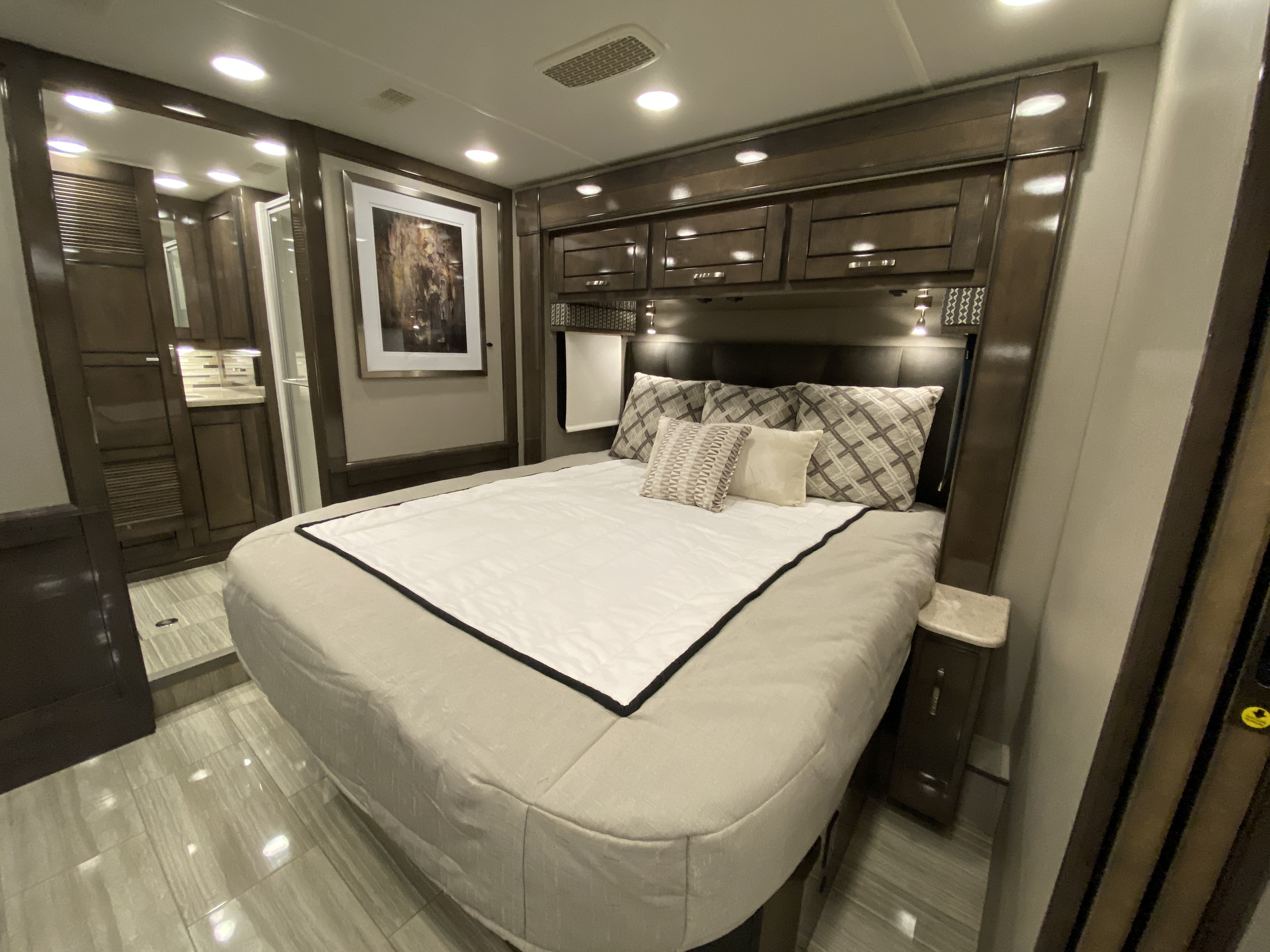 Luxurious RV bedroom setup for your RV rental, featuring a comfortable bed, modern cabinetry, and an adjoining sleek bathroom.. Entegra Coach Reatta 2021