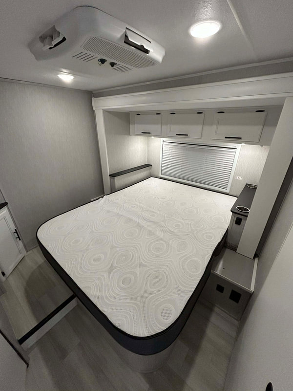 Comfortable RV rental bedroom with a large bed, ceiling AC unit, overhead storage, and window blinds.. Forest River Coachmen Cross Trail XL 2024