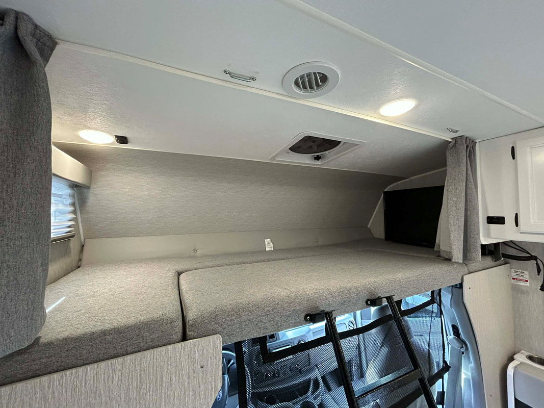 Rv rental interior: comfy grey cab-over bunk bed with a ladder, window, TV, and bright overhead lights.. Forest River Coachmen Cross Trail XL 2024