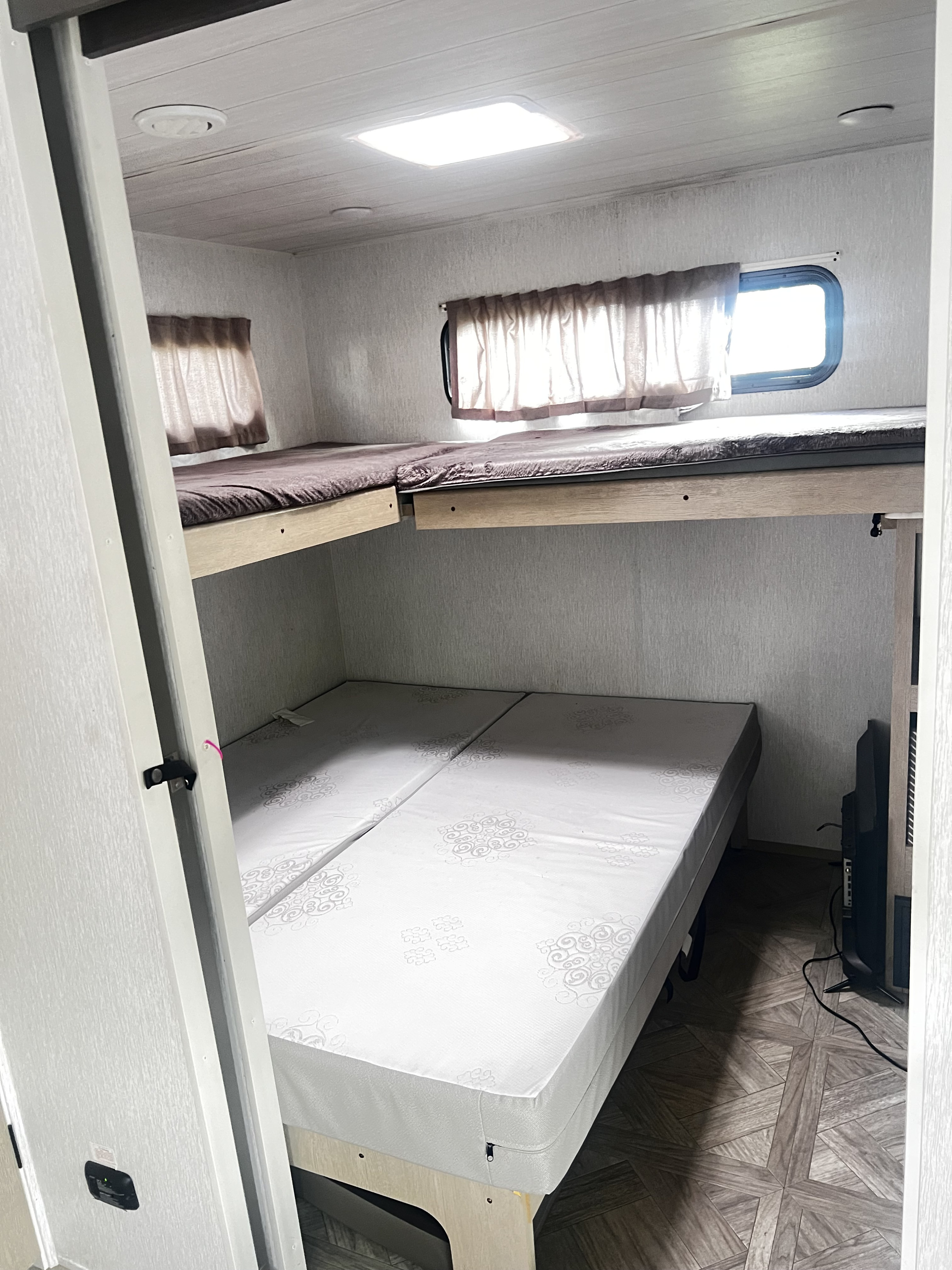 Inside an RV rental: a bunk room with upper and lower beds, windows, and a TV. Ideal sleeping space for travelers.. Forest River Salem FSX Plantium 2022