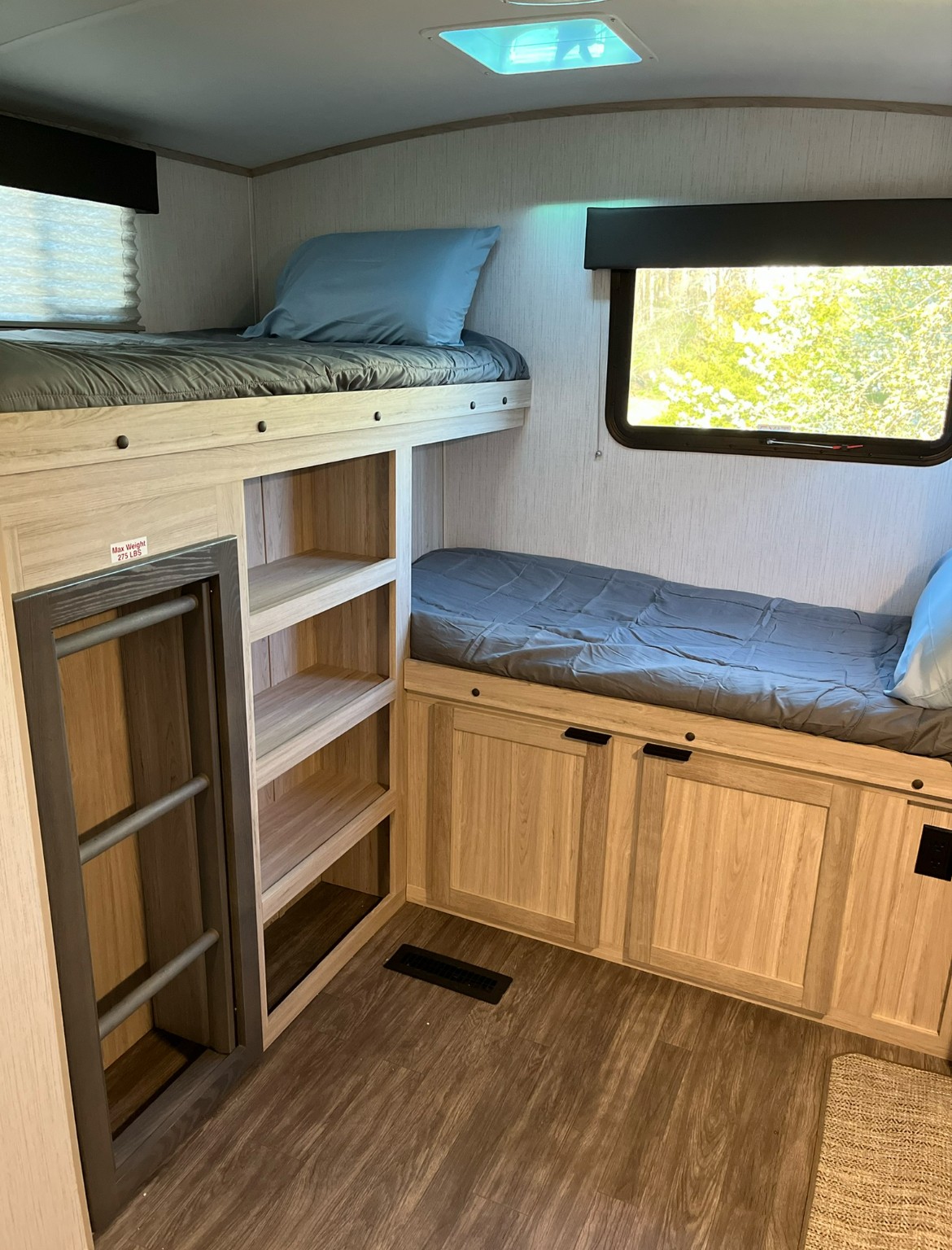 RV rental interior featuring bunk beds with blue pillows, built-in storage, a window with a green view, and wood-look flooring.. Cruiser RV Shadow Cruiser 2022