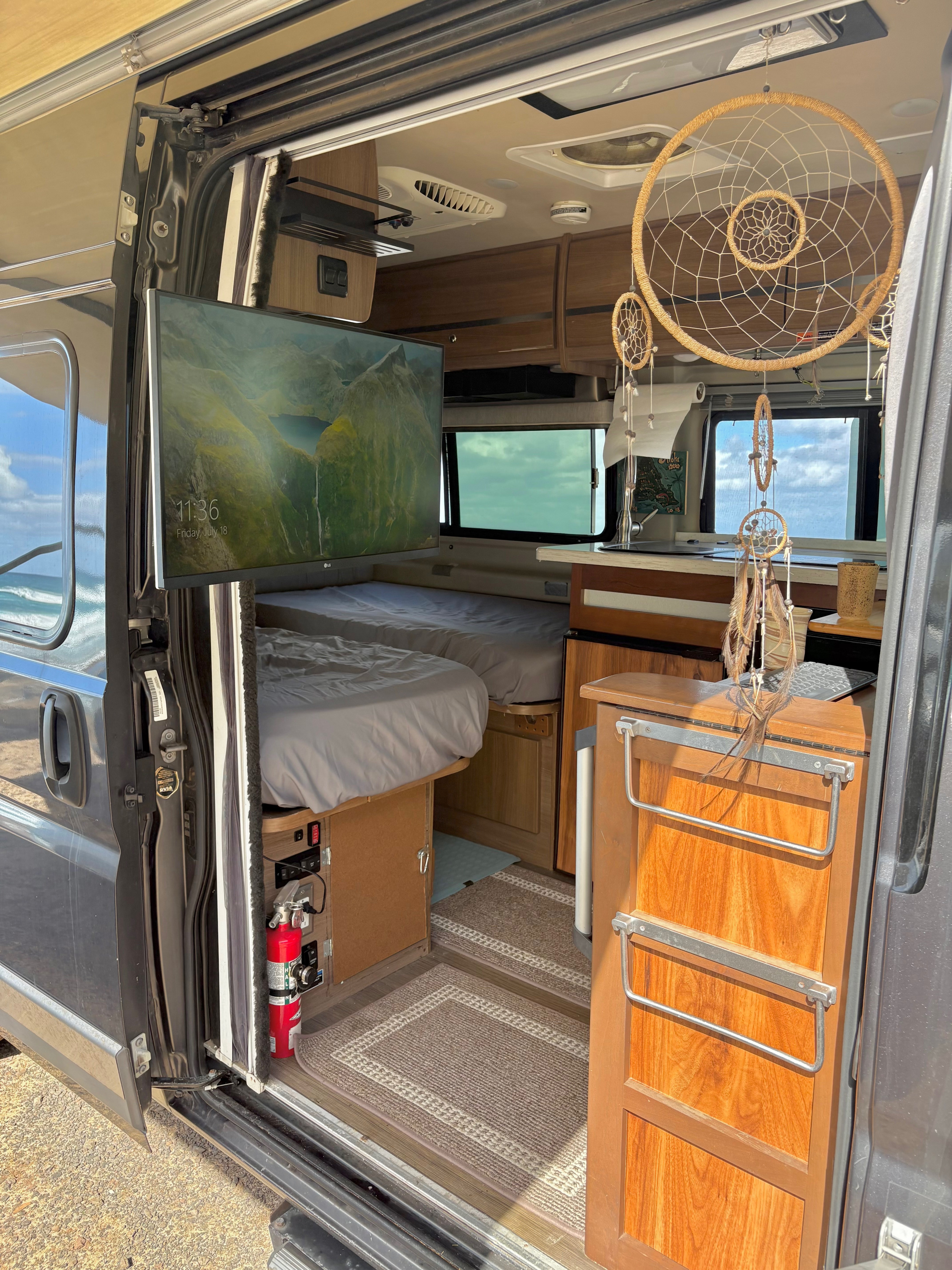 Cozy rv rental interior with beds, TV, kitchen, and dreamcatchers, ready for adventure by the ocean.. Winnebago Travato 2017