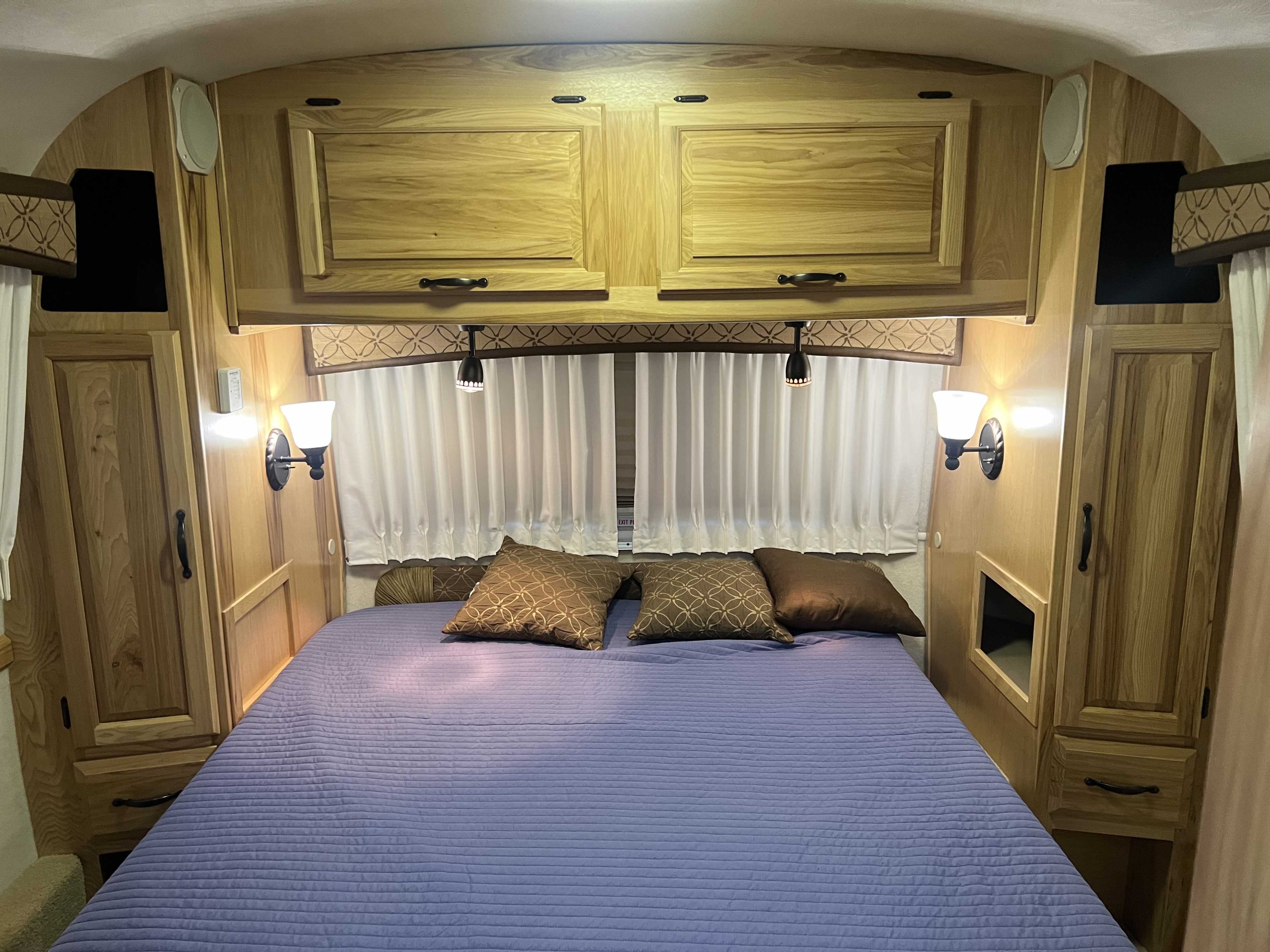 Cozy RV rental bedroom featuring wooden cabinets, a comfortable bed with a blue quilt, and warm lighting.. Airstream Classic 2012