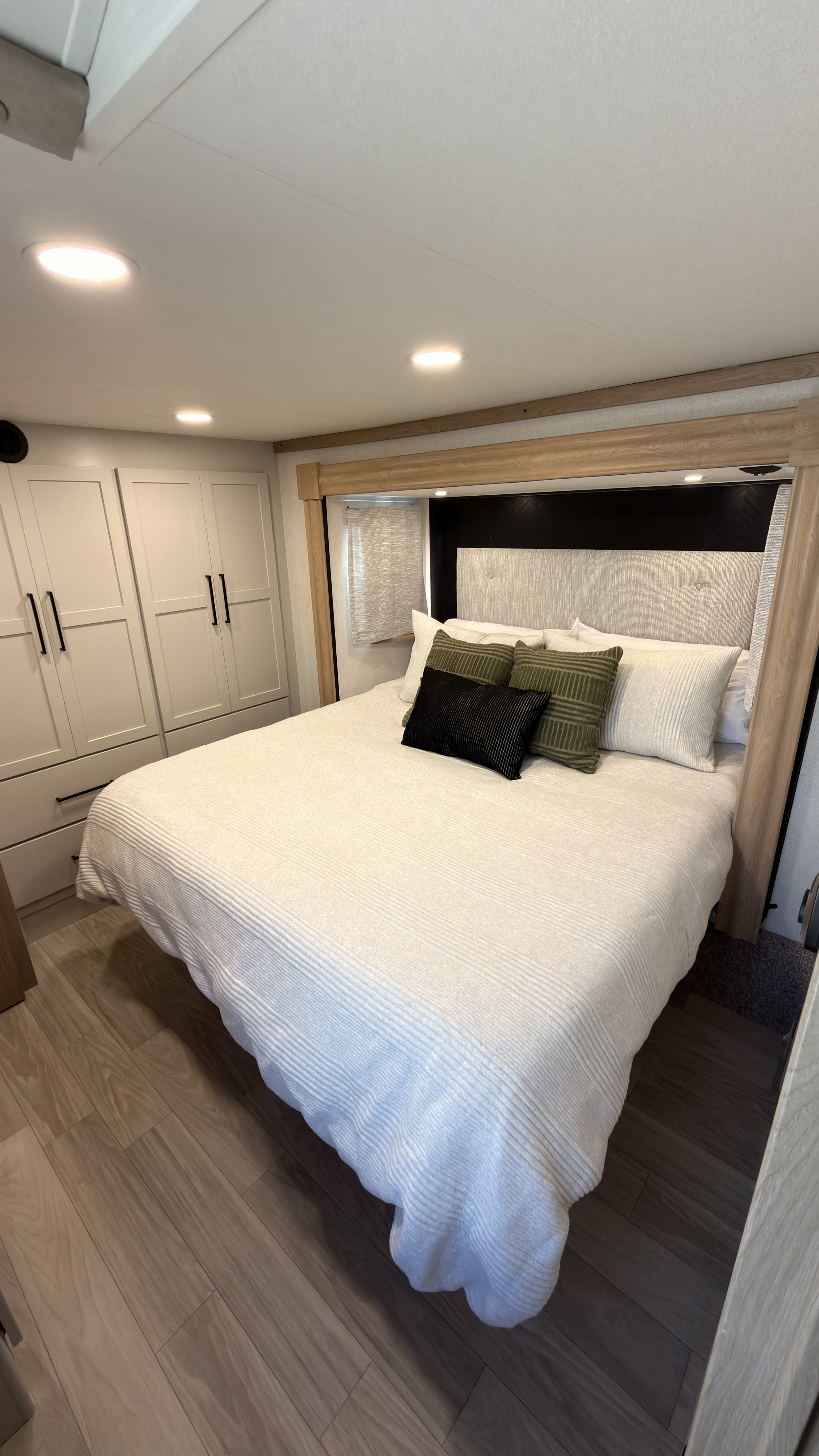 A bright, modern RV rental bedroom featuring a queen bed with crisp white bedding, decorative pillows, and built-in storage.. Forest River Sierra 3990FL 2025