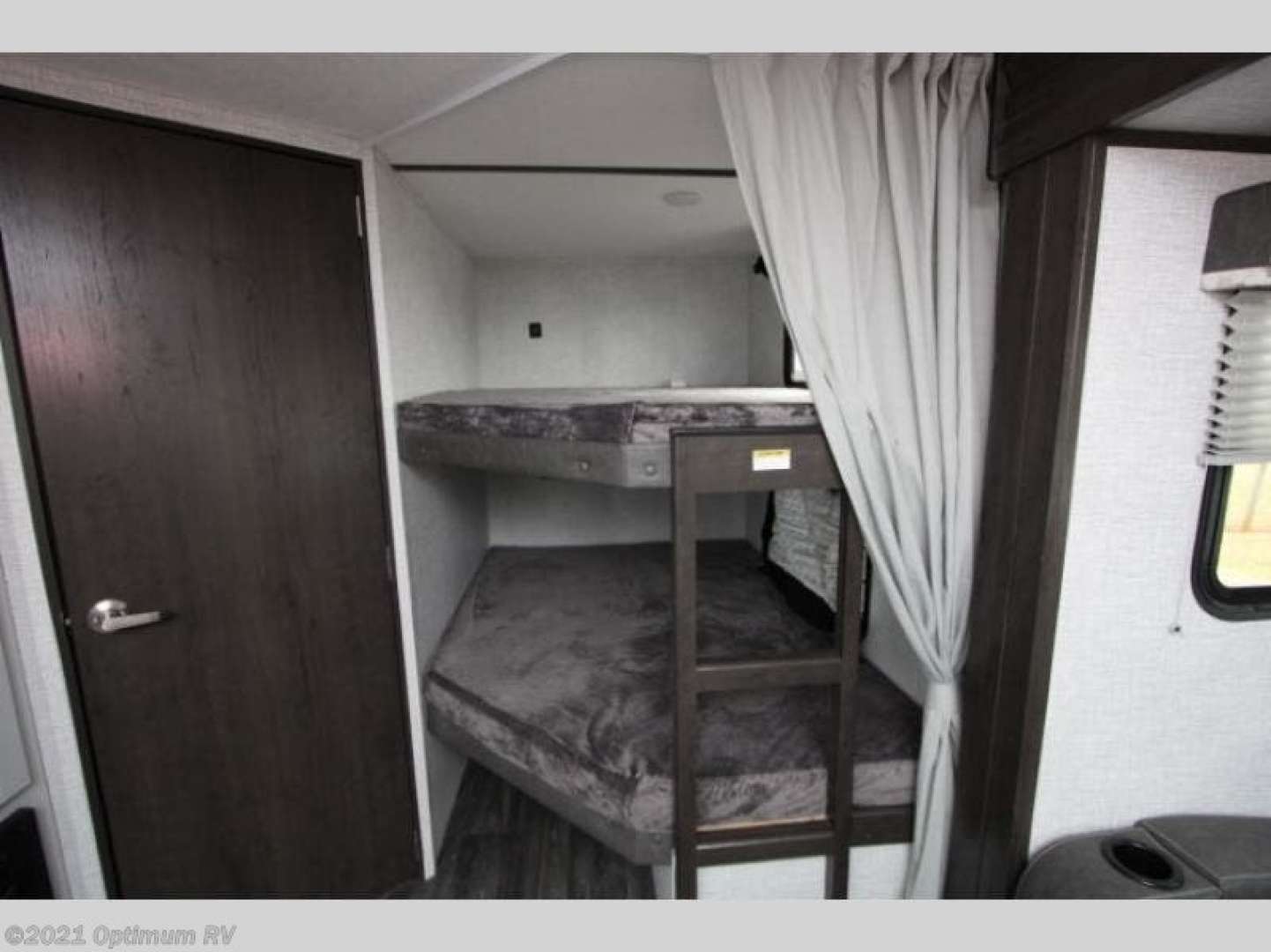 Compact RV rental interior featuring cozy bunk beds with a ladder, door, and privacy curtain for comfortable travel.. Keystone RV Bullet Crossfire 2021