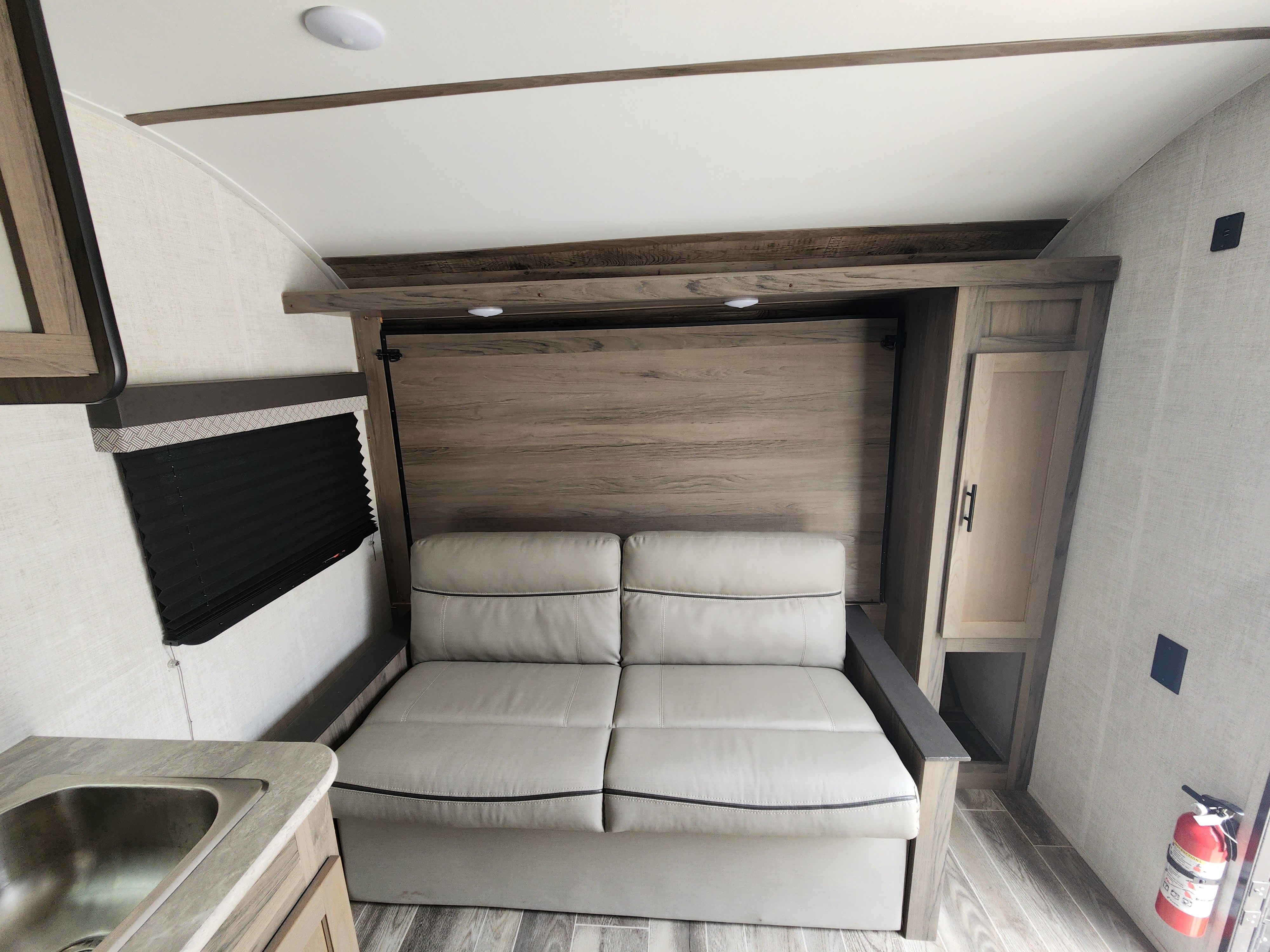 RV rental interior featuring a light-colored sofa (likely a pull-out or murphy bed), a small kitchen sink, and wooden storage.. Gulf Stream Ameri-Lite Super Lite 2022