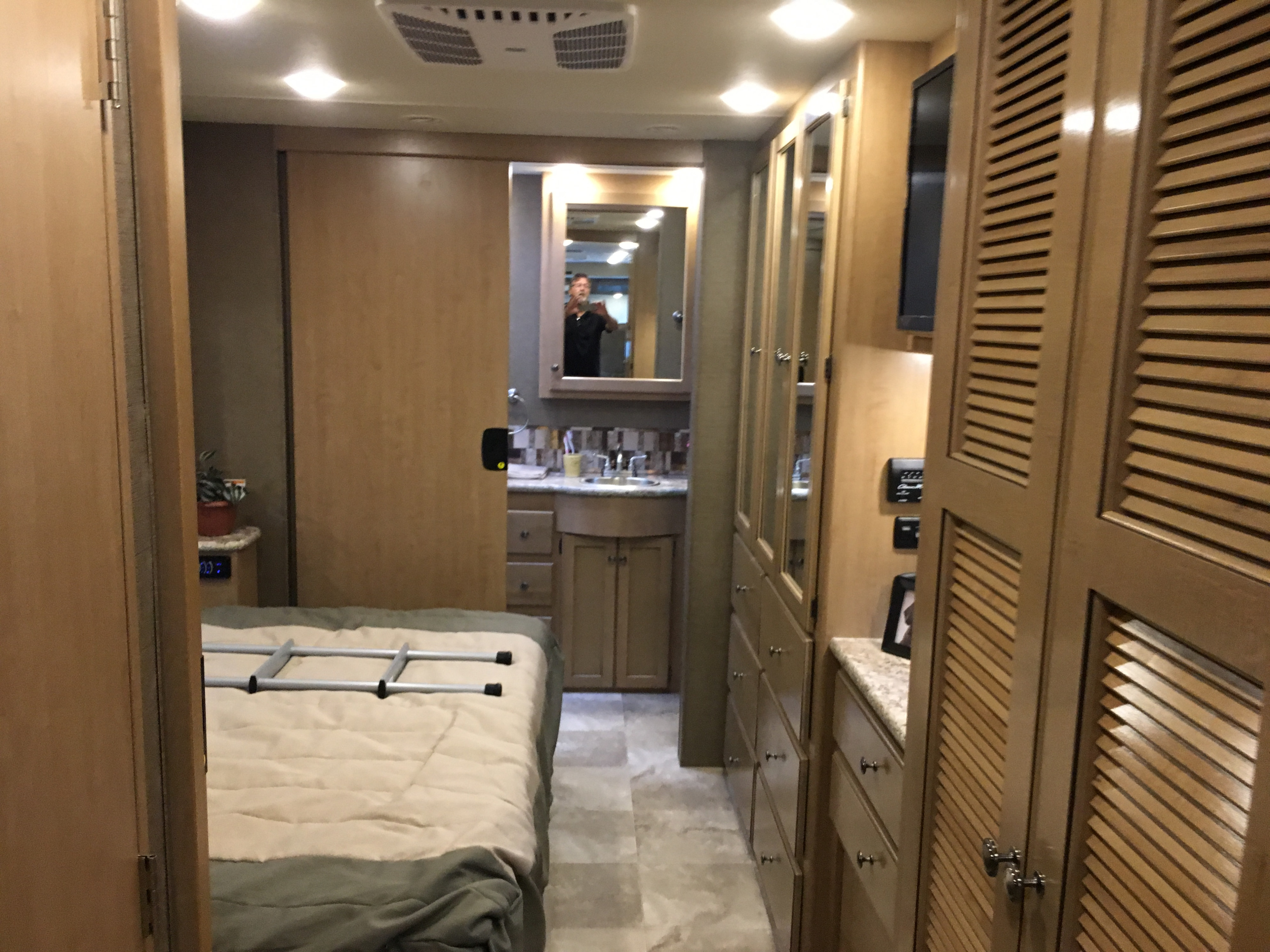 View into an RV rental's cozy bedroom and connected bathroom vanity. Complete with storage cabinets and a mounted TV.. Thor Windsport 2018