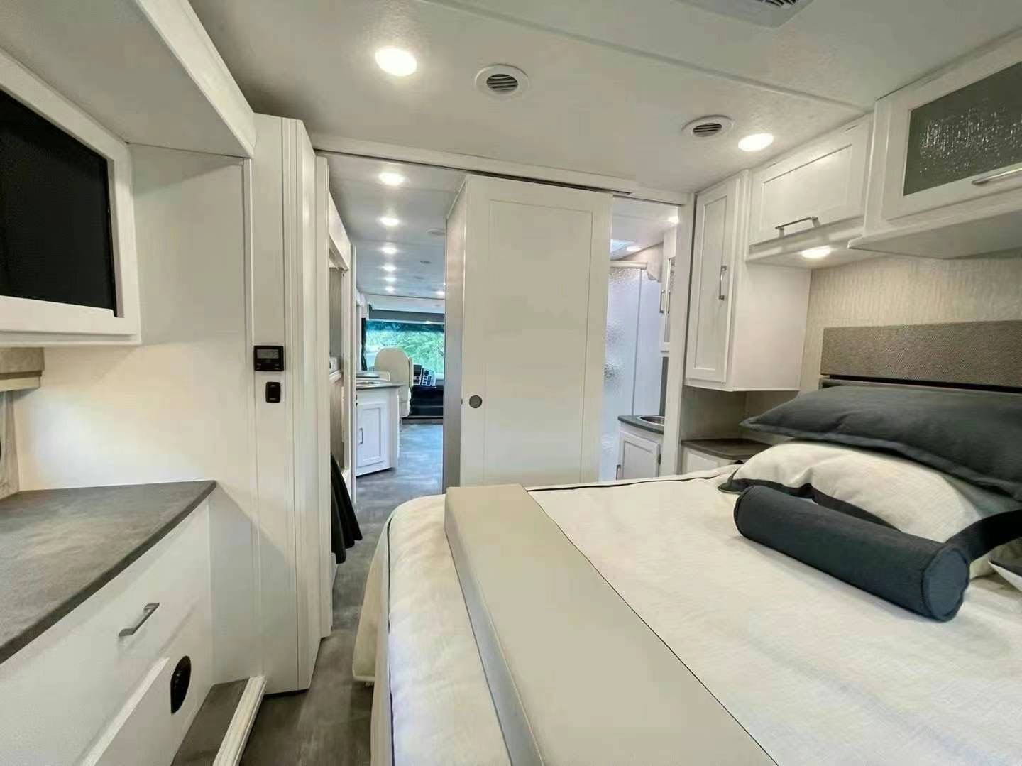 Modern RV rental interior with a bedroom, en-suite bathroom, and view to the front living area. Clean and functional design.. Coachmen Pursuit BH31 2023