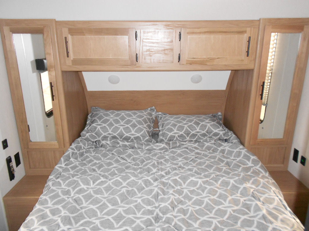 Cozy RV rental bedroom with light wood cabinets, mirrored wardrobes, and a patterned comforter.. Forest River Cherokee Grey Wolf 2025