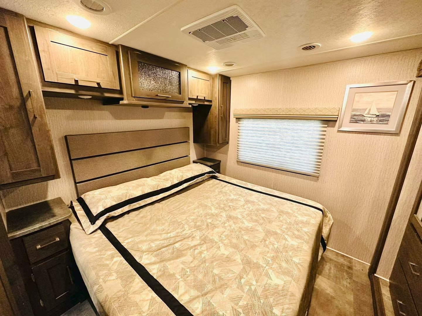 Comfortable RV rental bedroom with a tan patterned bed, upholstered headboard, wood cabinets, and window with blinds.. Coachmen Pursuit 31BH 2023