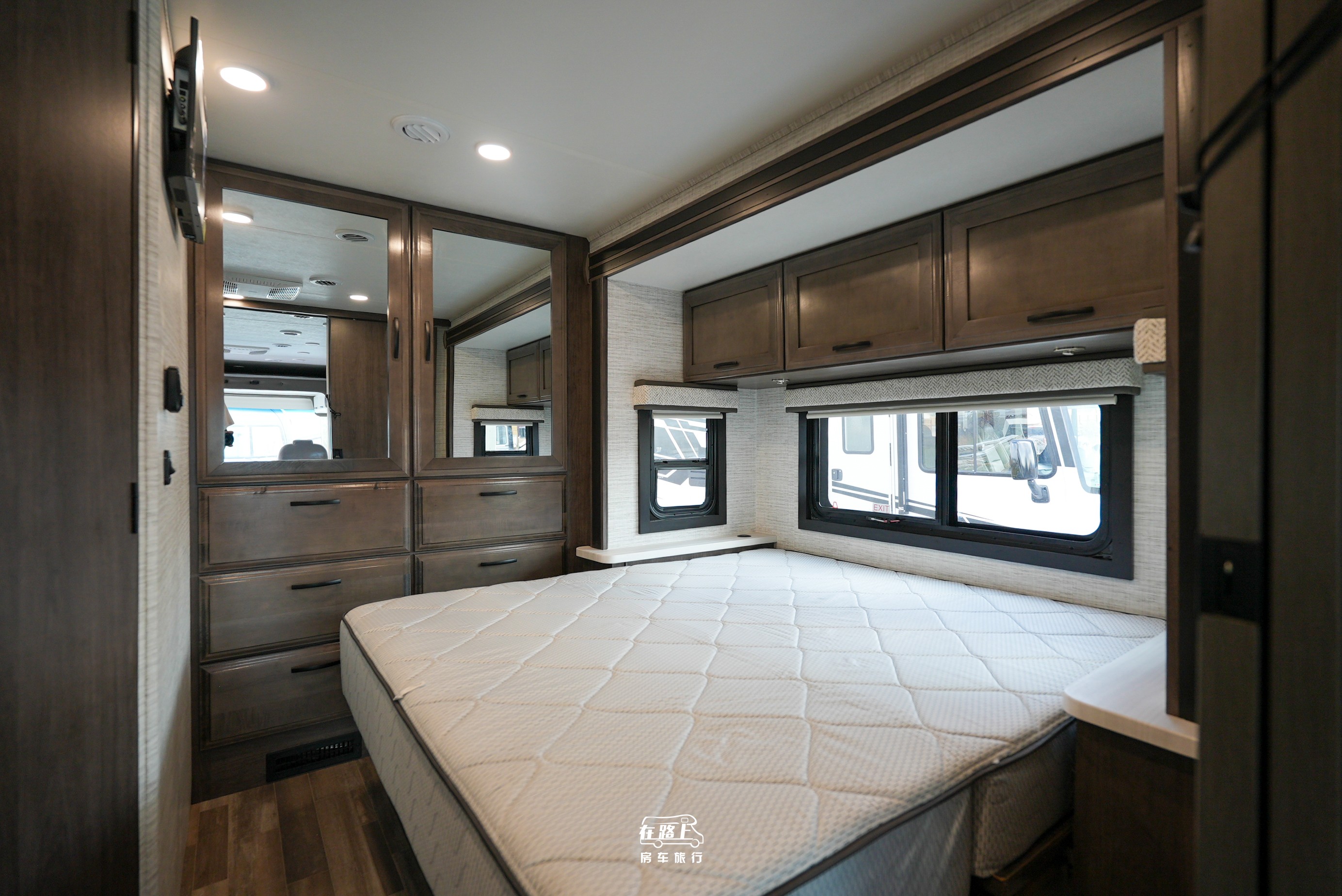 Spacious RV rental bedroom features a comfy bed, overhead cabinets, dresser with mirrors, and large windows for comfortable travel.. Jayco Travel Supreme A Series 27A 2025