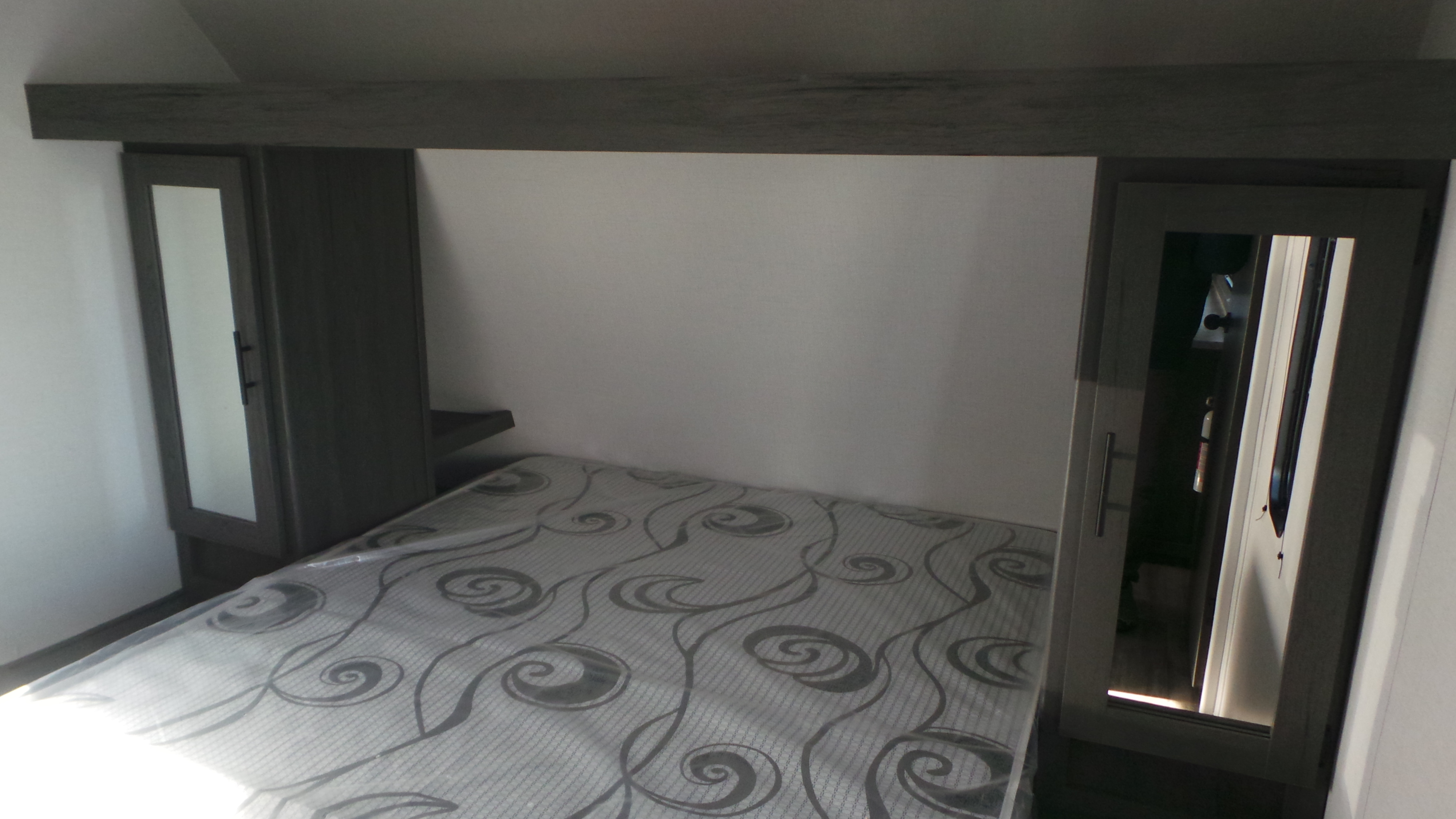 Experience comfort in this RV rental bedroom: bed with patterned mattress (in plastic), overhead shelf, and mirrored storage cabinets.. Colorado Colorado Trailer 2025