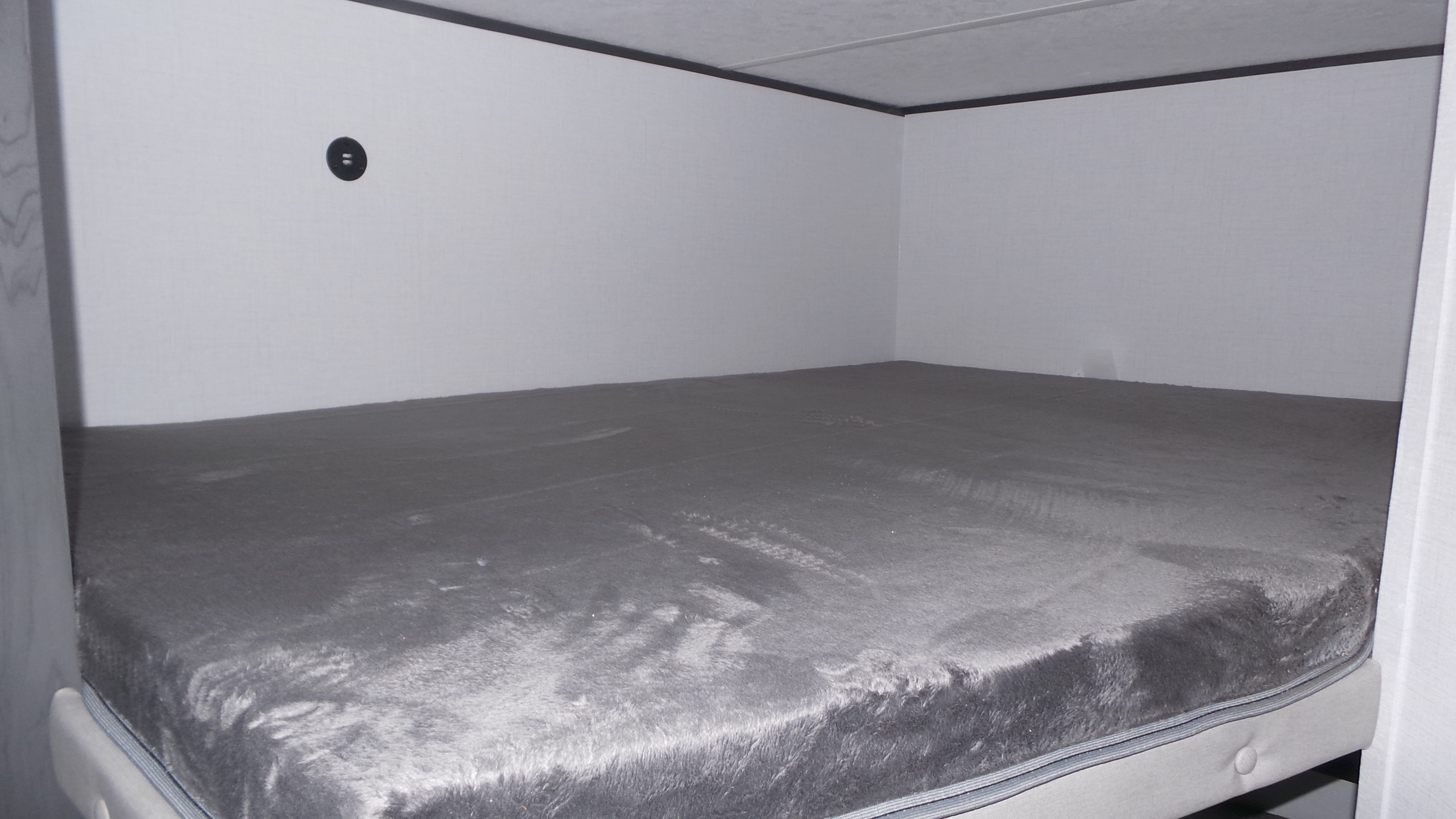 RV rental bunk bed with a grey fuzzy mattress, white walls, and a black circular outlet.. Colorado Colorado Trailer 2025