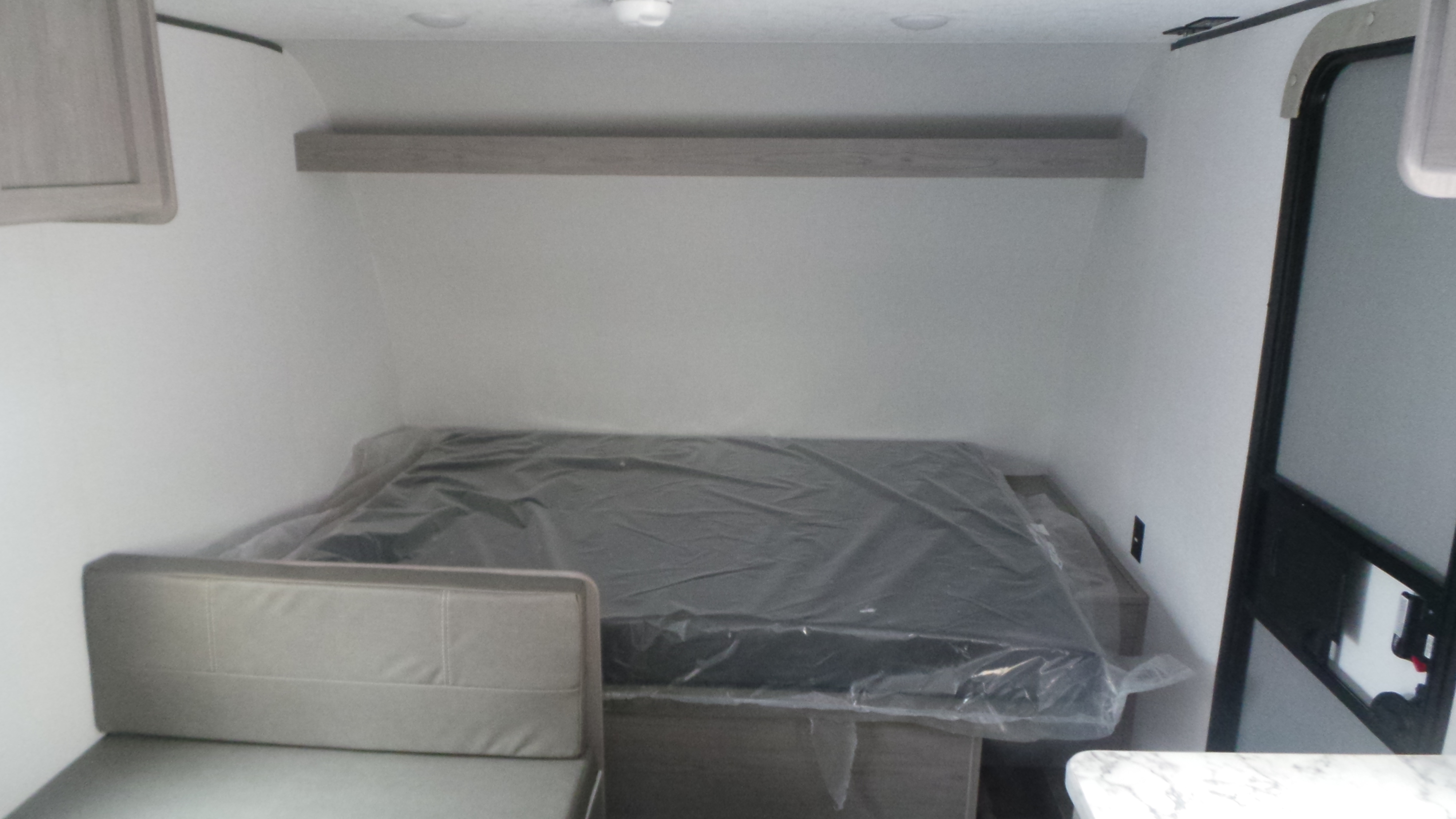 RV rental interior with a bed (still in plastic), a small couch, and a wall shelf, ideal for compact travel.. Colorado Colorado Trailer 2025