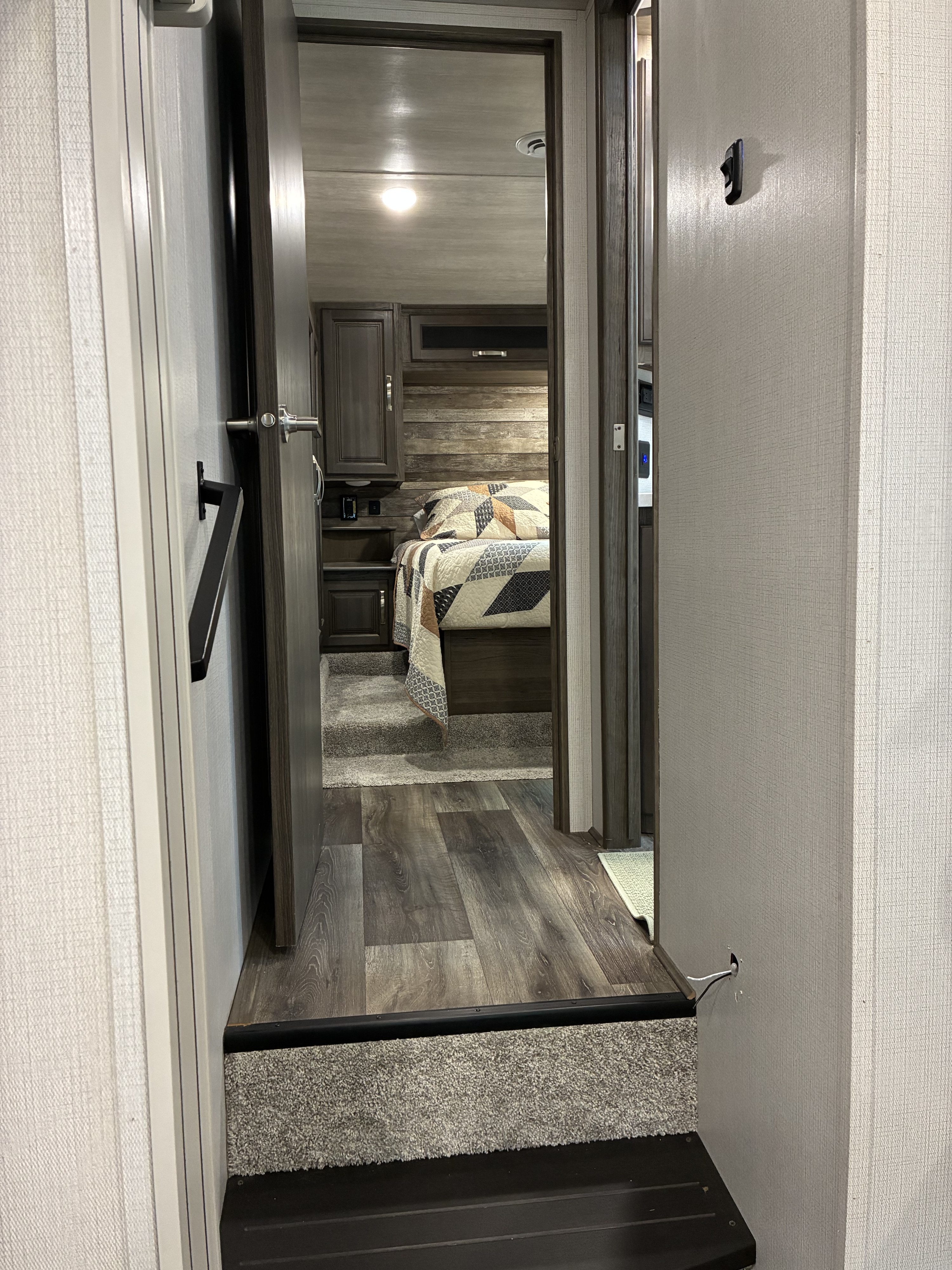 RV rental interior: Hallway leading to a cozy bedroom with wood floors, carpeted steps, and a patterned bed.. Keystone RV Cougar 2022