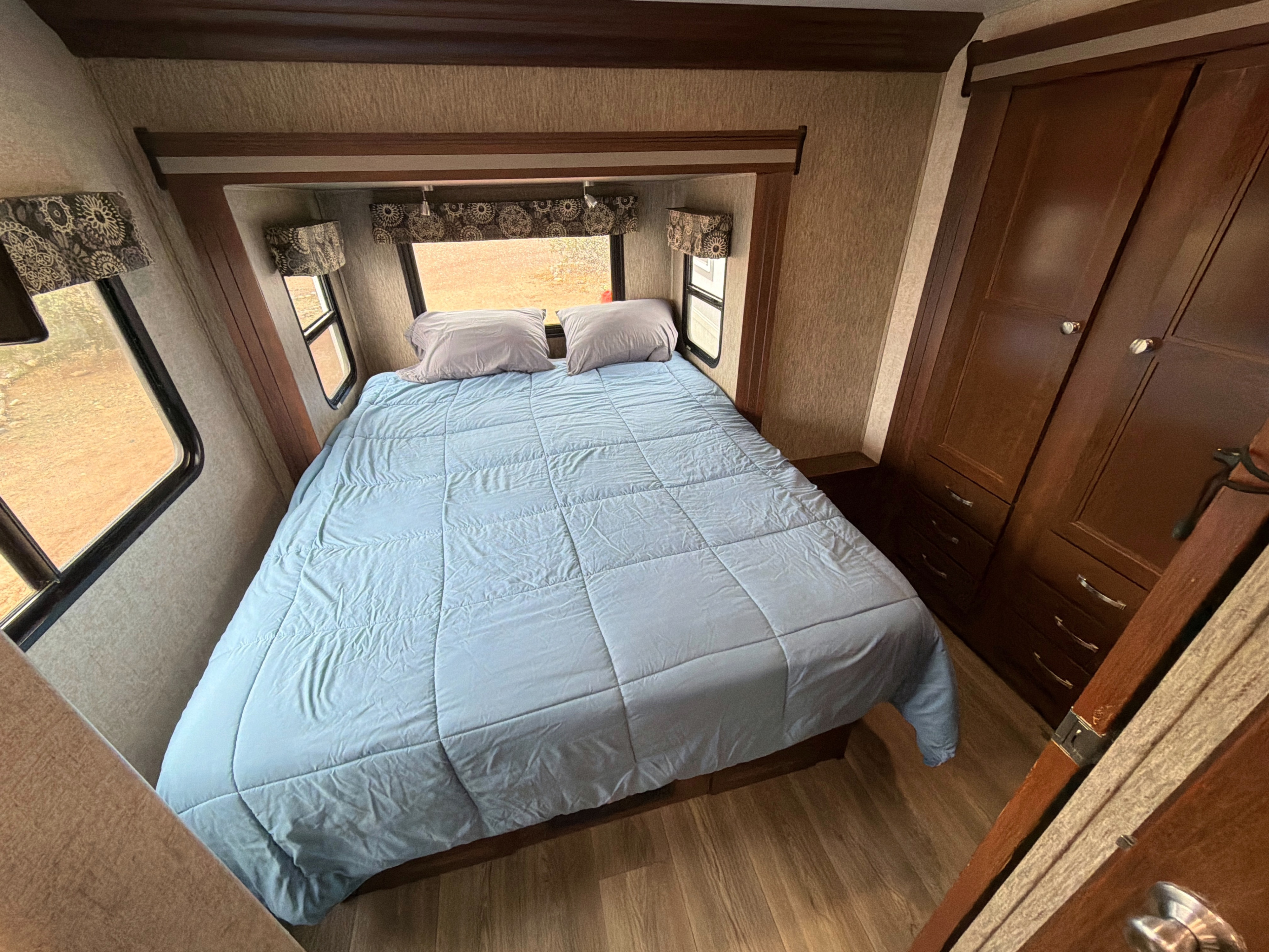 An RV rental bedroom with a large bed, light blue comforter, multiple windows, and ample wooden wardrobe storage.. Forest River Sunseeker 2017