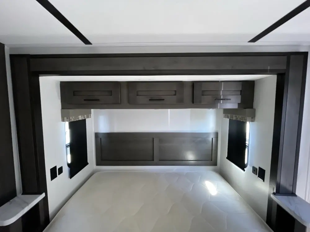 Compact rv rental bedroom: comfortable bed, dark wood headboard, overhead storage, and windows. Perfect for travel.. FR3 FR3 Motorhome 2024