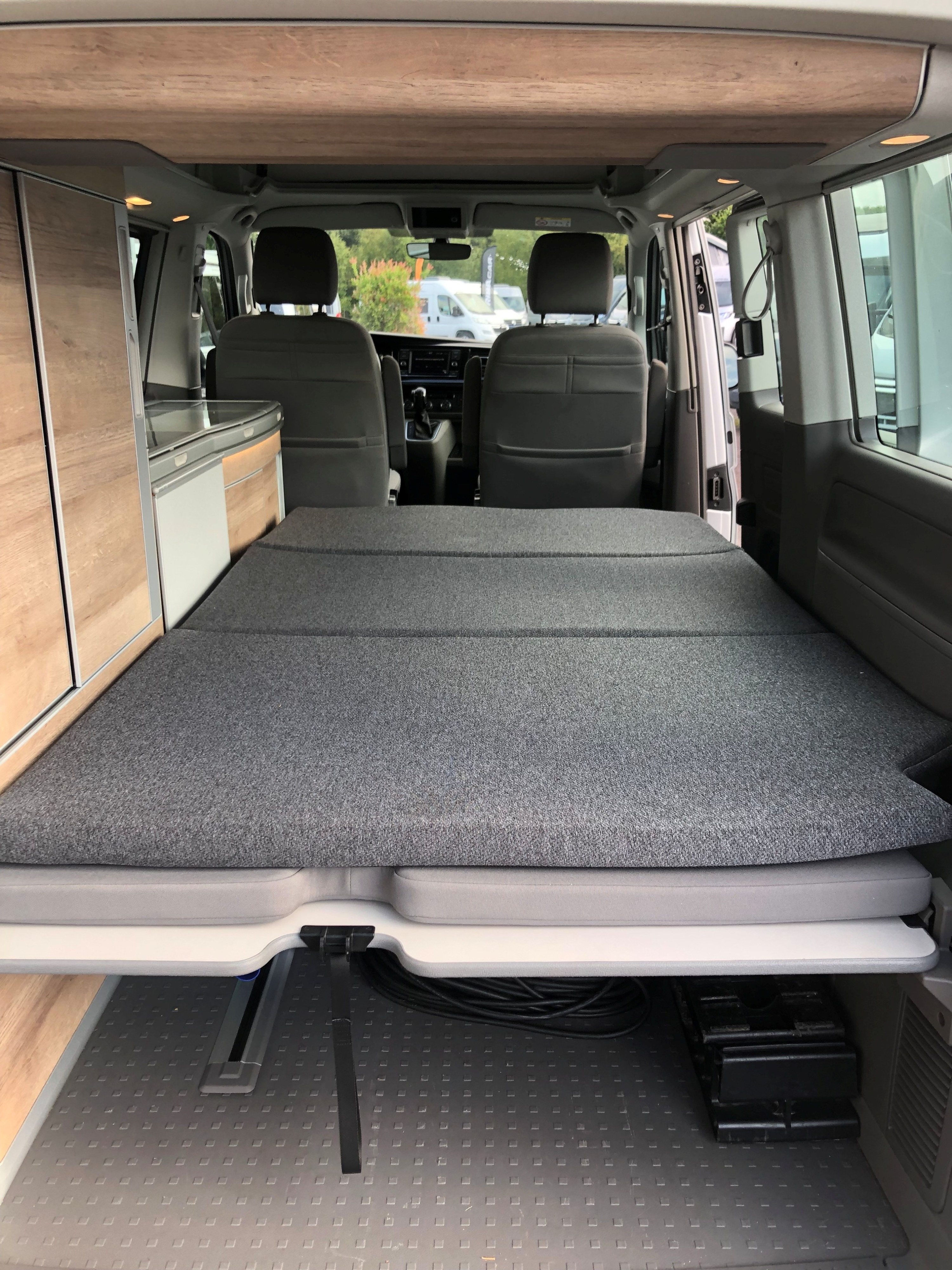 Enjoy your next rv rental in this camper van! Interior view shows a comfortable fold-down bed, compact kitchen, and front seats.. Volkswagen California Coast T6 2023