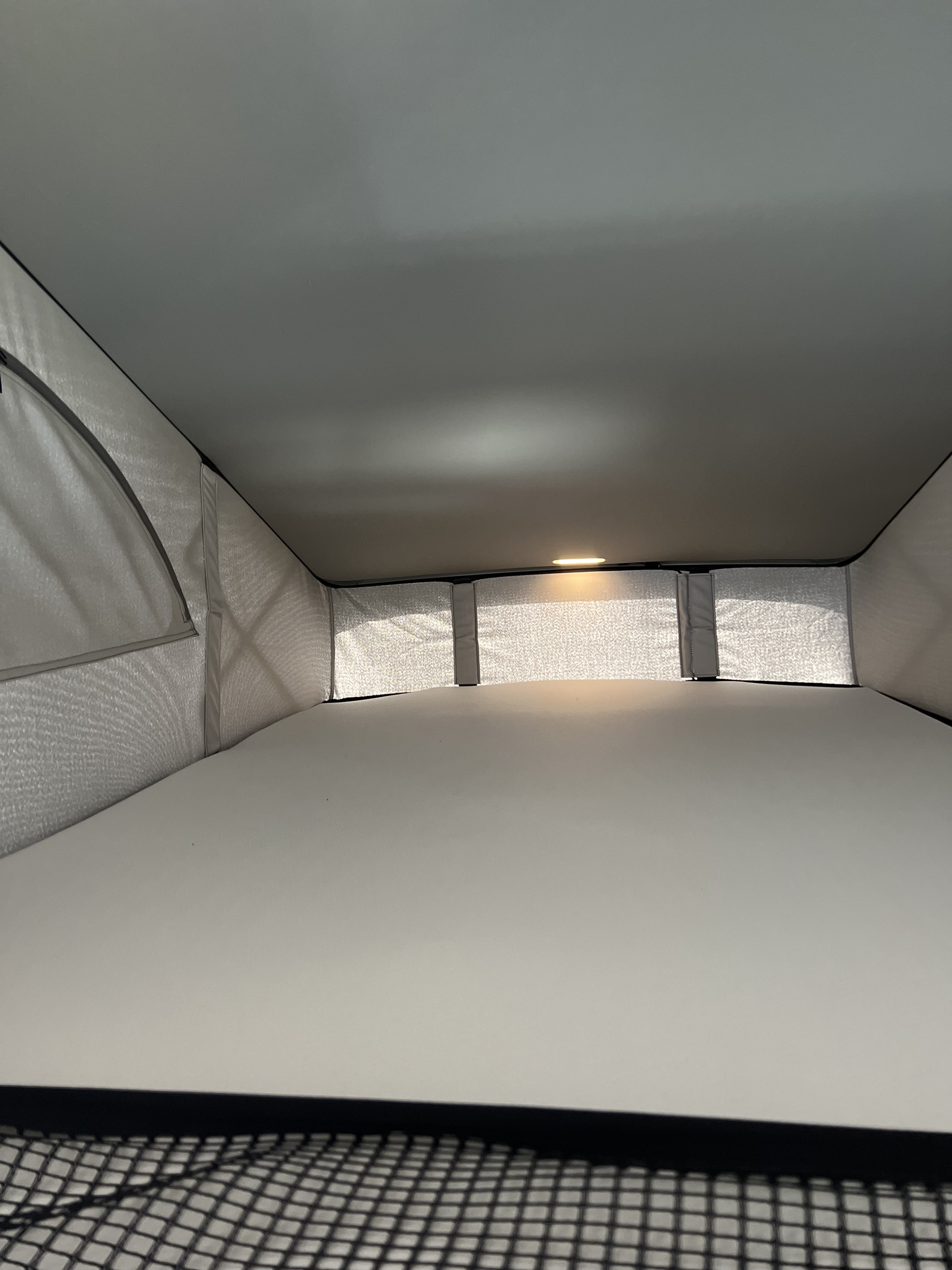 Interior view of a cozy pop-top sleeping area in an rv rental, featuring a white mattress, mesh walls, and ambient lighting.. Volkswagen California Coast T6 2023