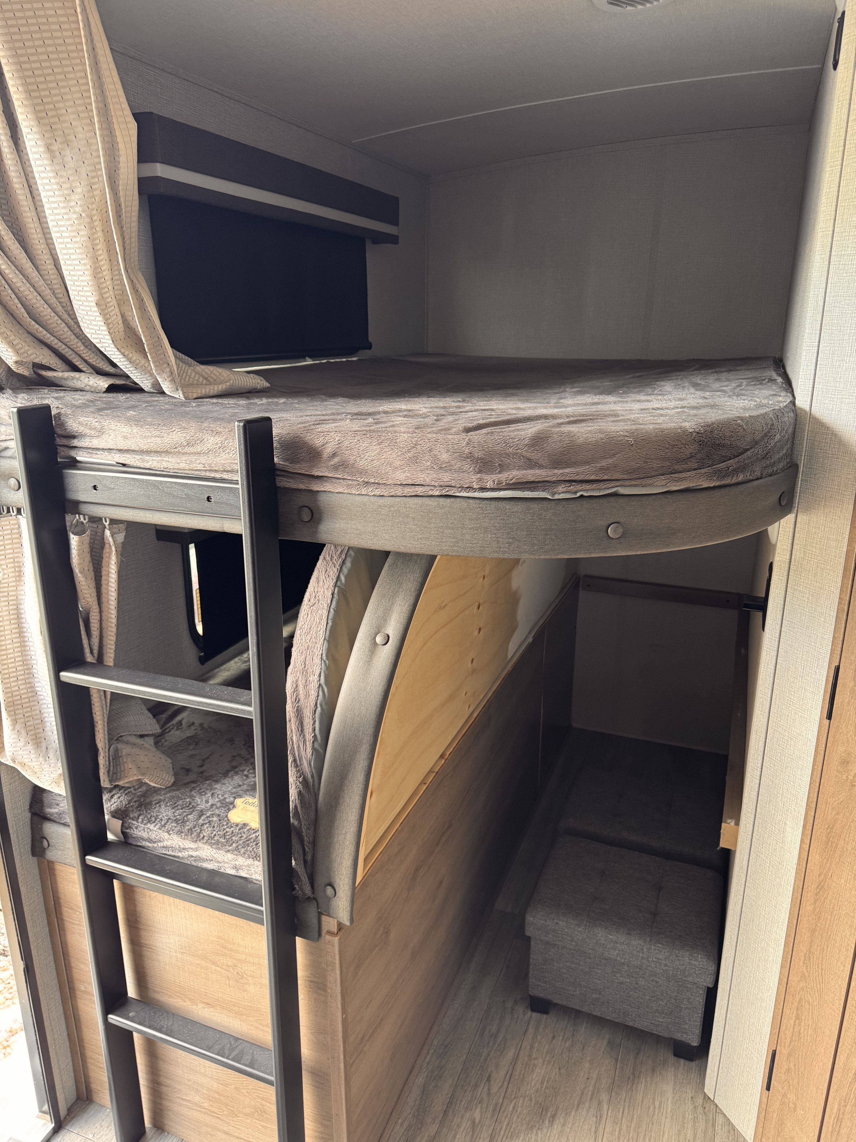 RV rental bunk beds: an upper sleeping area with ladder, and a lower versatile space featuring seating ottomans and storage.. Grand Design Imagine 2023