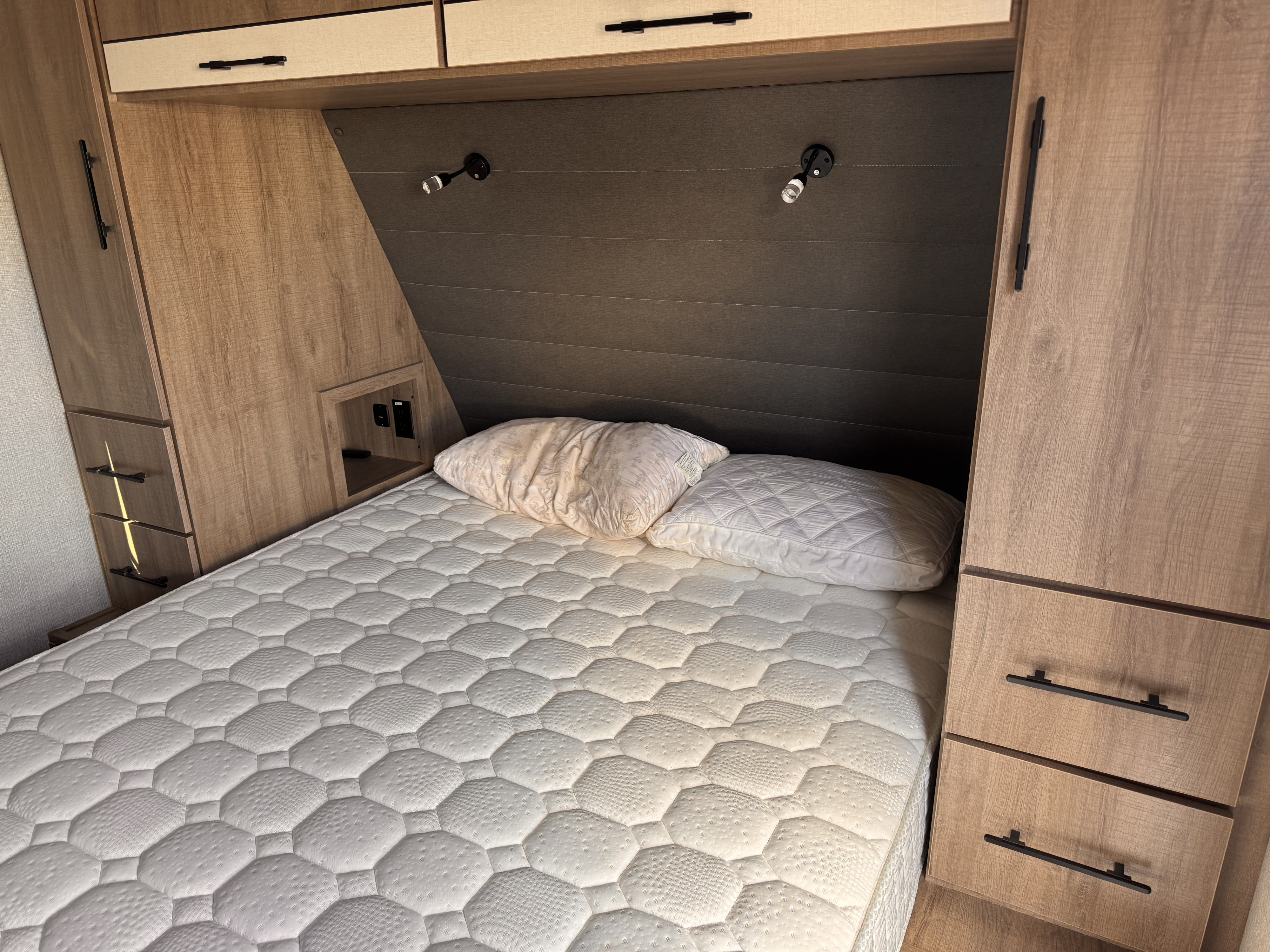 Comfortable RV rental bedroom featuring a quilted mattress, pillows, built-in storage, and reading lights.. Grand Design Imagine 2023