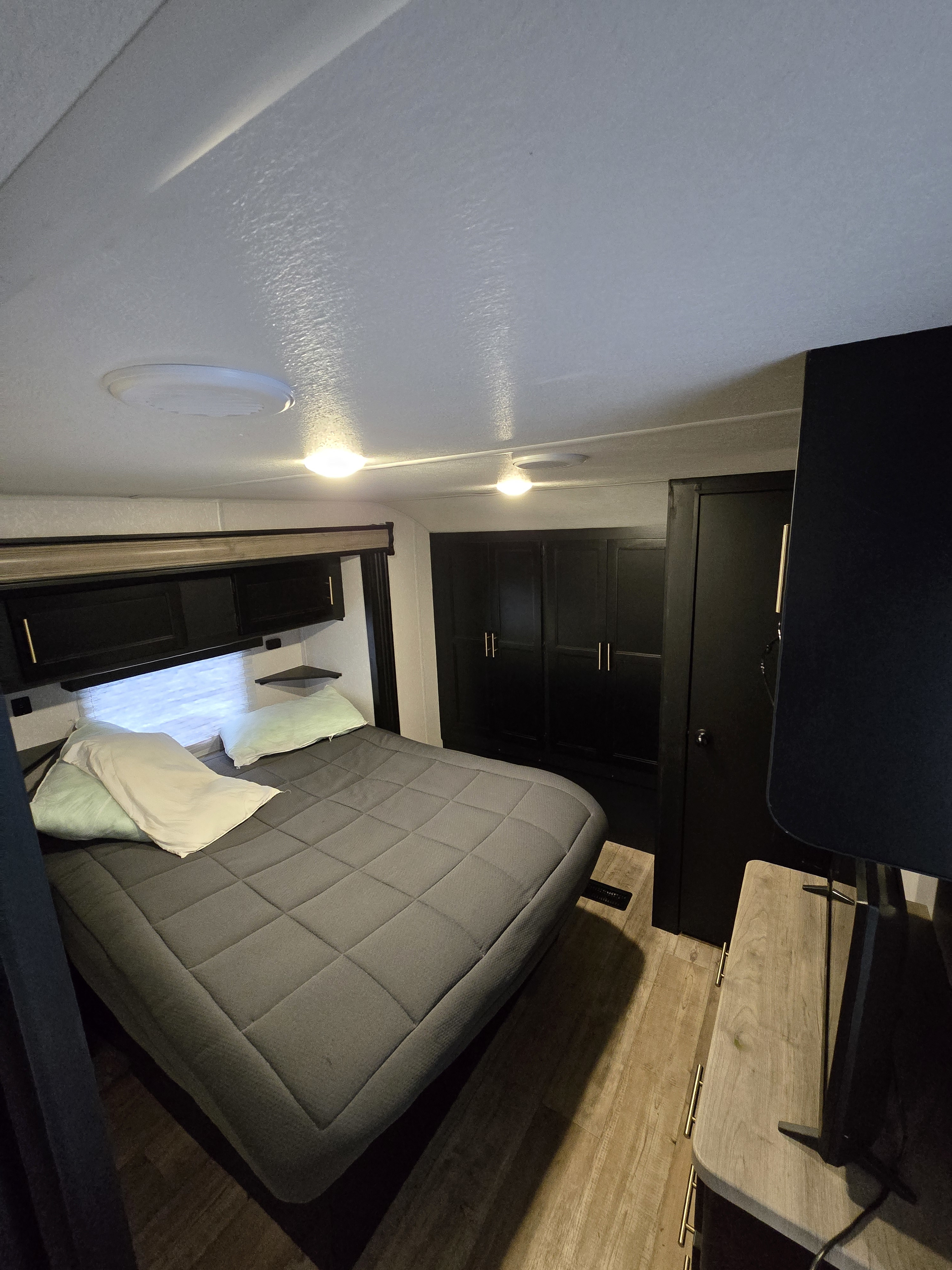 Cozy bedroom interior of an RV rental with a queen bed, overhead cabinets, and a dresser with a TV.. Forest River Cherokee 2022