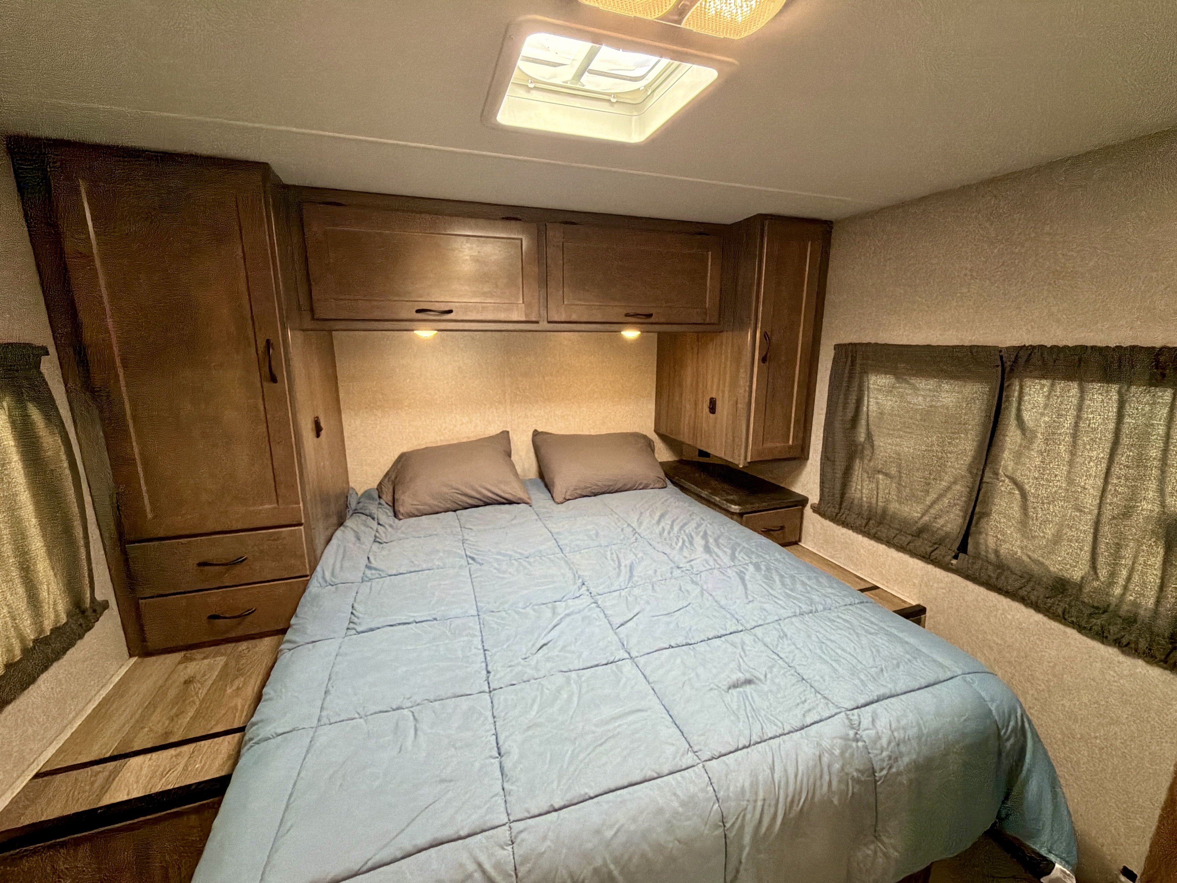 Cozy RV rental bedroom features a bed with blue comforter, ample wooden cabinets, and a skylight for natural light.. Winnebago Minnie Winnie 2020