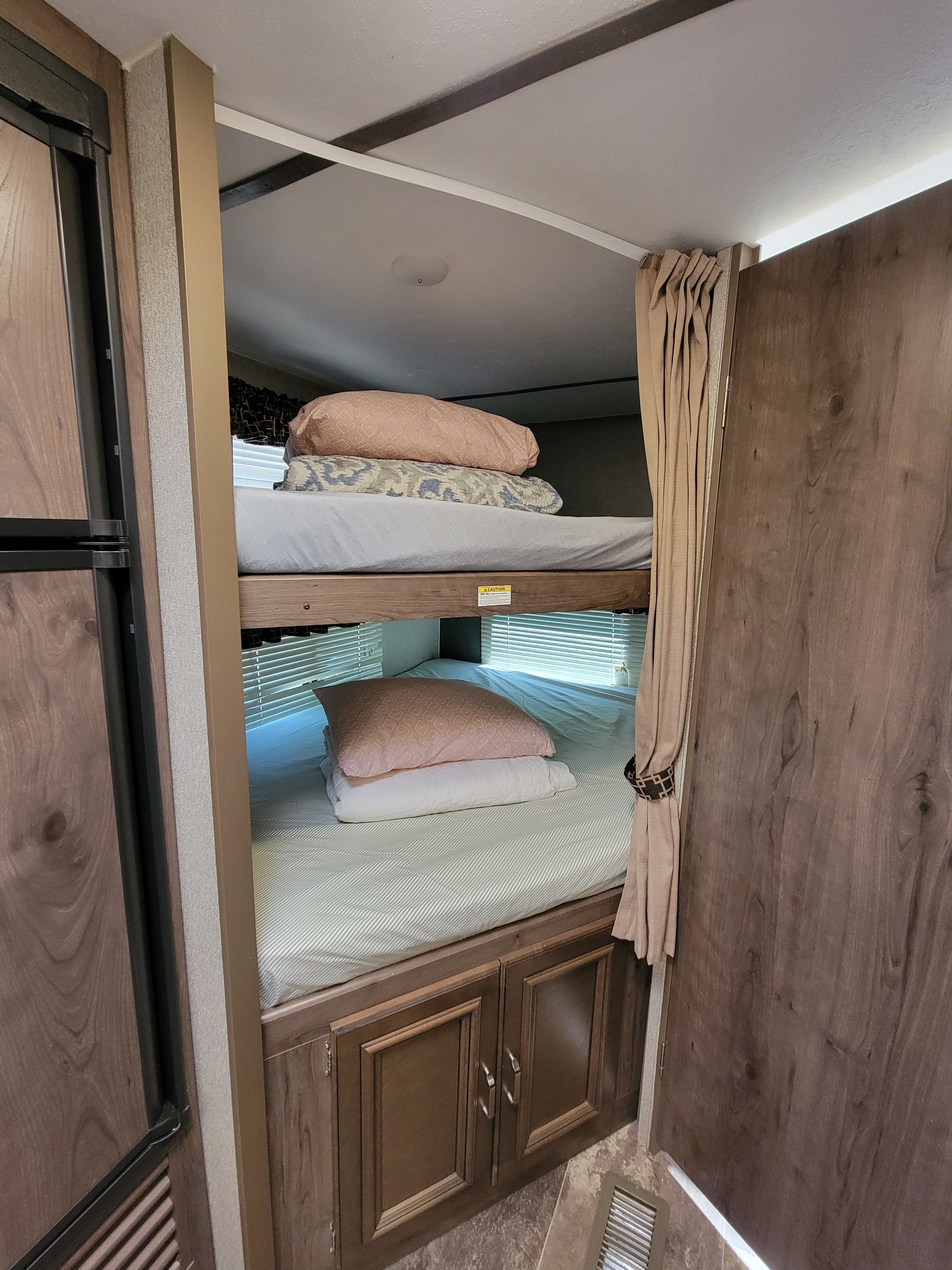 RV rental sleeping area with cozy bunk beds, bedding, window blinds, and storage cabinets.. Keystone RV Passport Grand Touring 2018