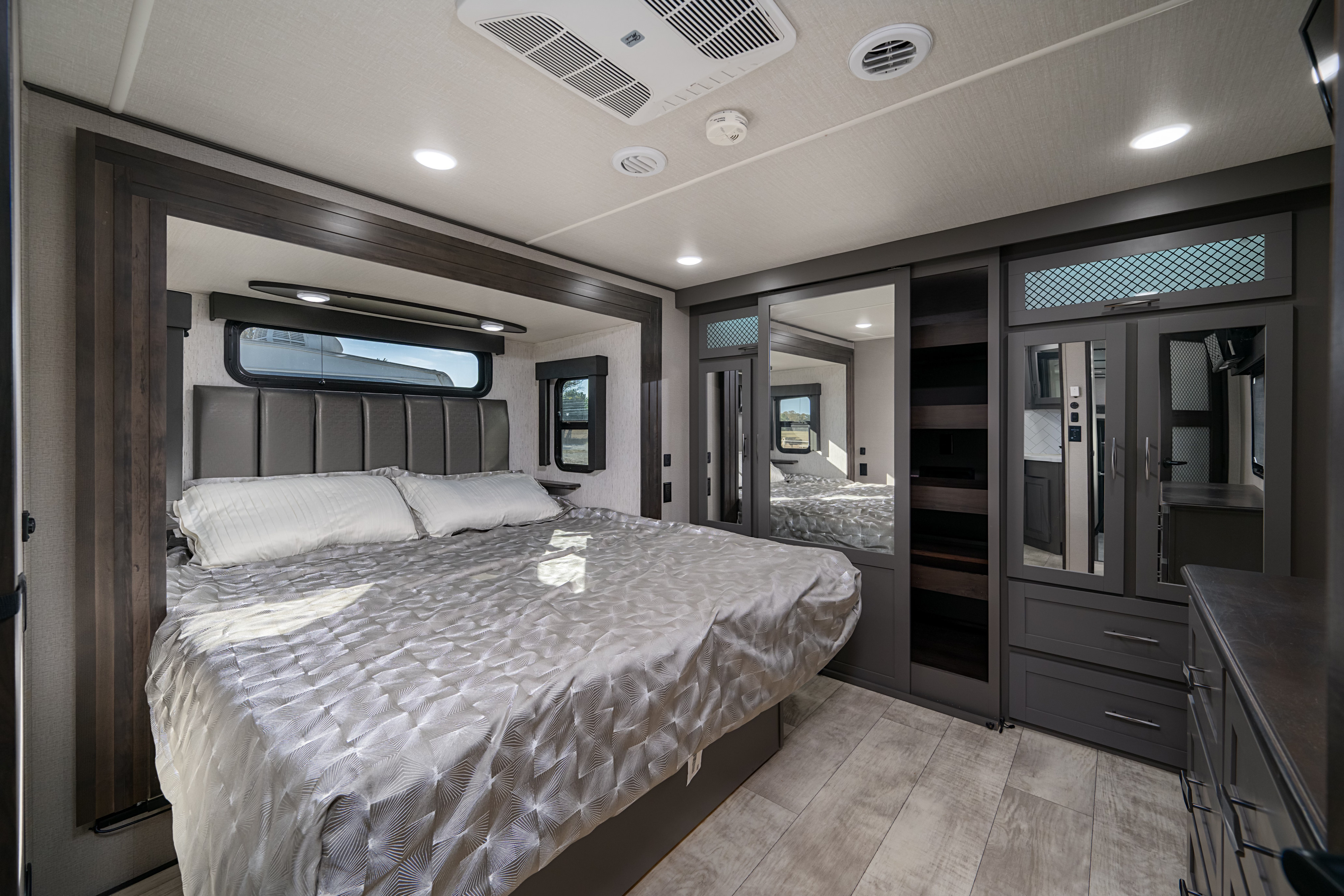 A spacious RV rental bedroom with a large bed, built-in mirrored wardrobe, and bright, modern decor for travel comfort.. Grand Design Momentum 2022
