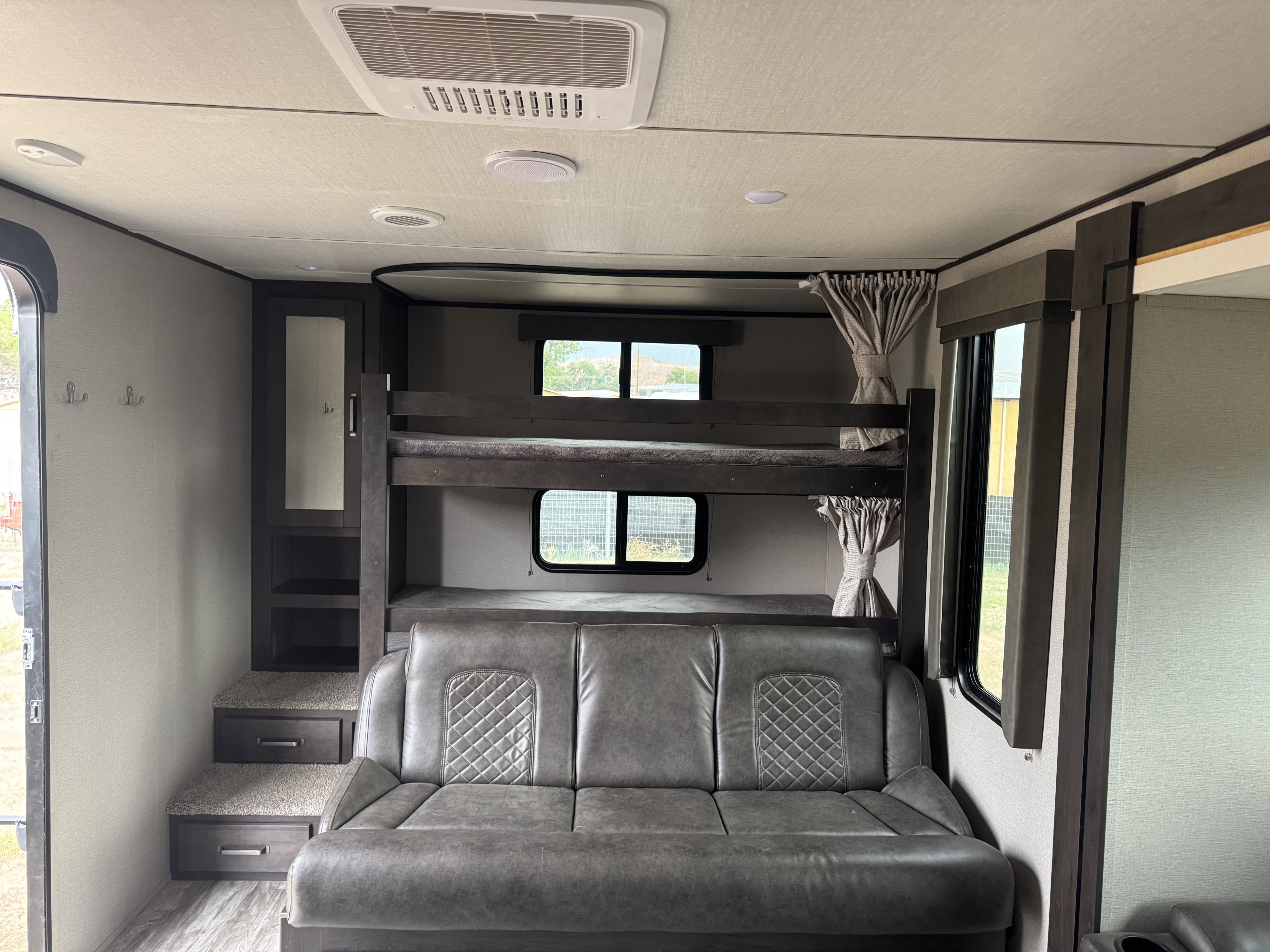 Inside an RV rental: bunk beds over a sofa, built-in storage, and steps with drawers. A comfy family space.. Grand Design Transcend Xplor 2021
