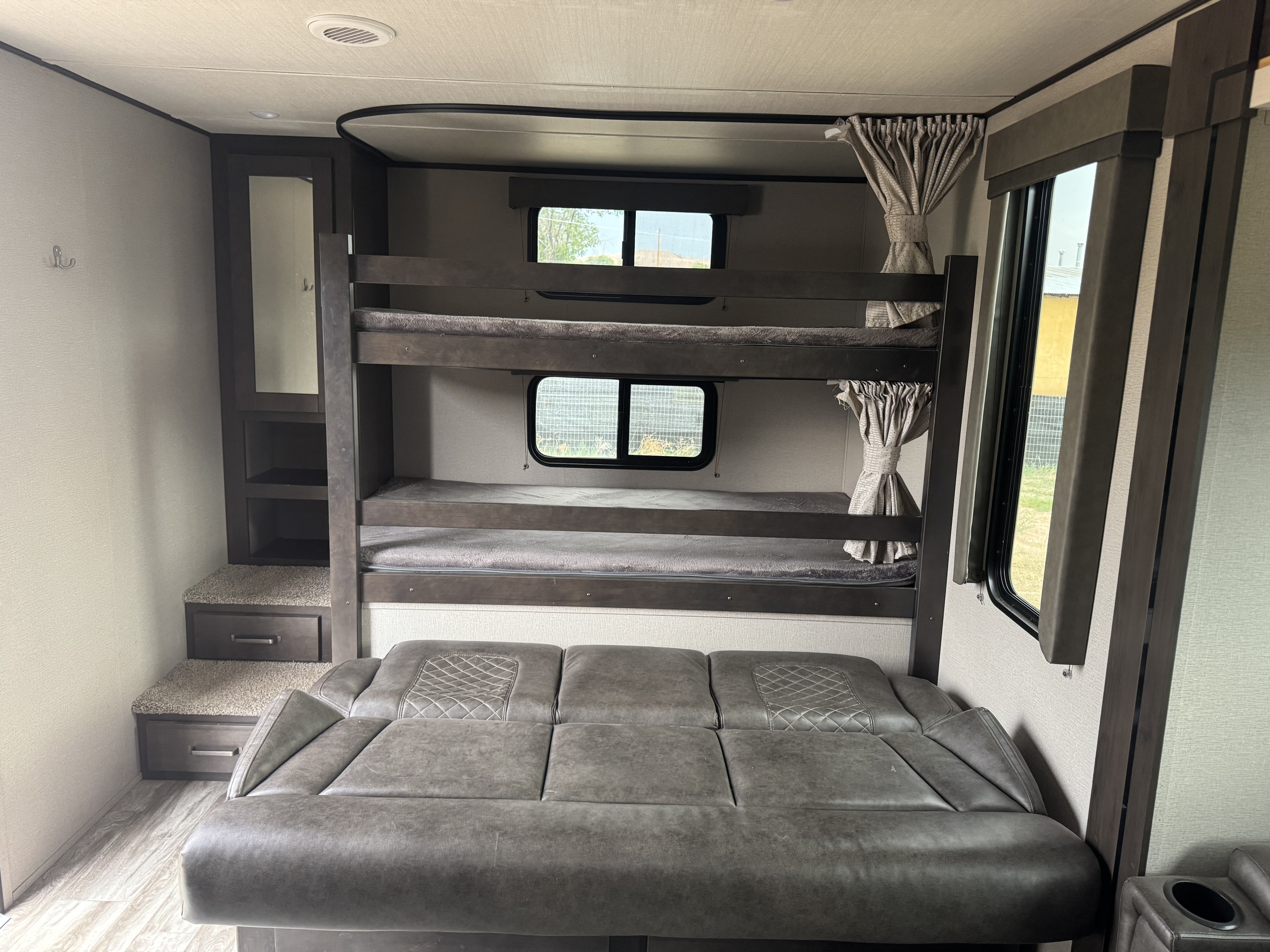 Inside this RV rental: A modern sleeping area with two dark-wood bunk beds, a gray sofa, and built-in storage.. Grand Design Transcend Xplor 2021