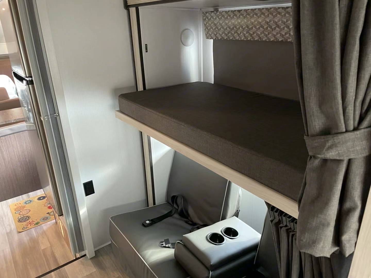 Inside an RV rental: a comfortable bunk bed setup with a lower seat, cupholders, and a privacy curtain.. Forest River Sunseeker LE 2022
