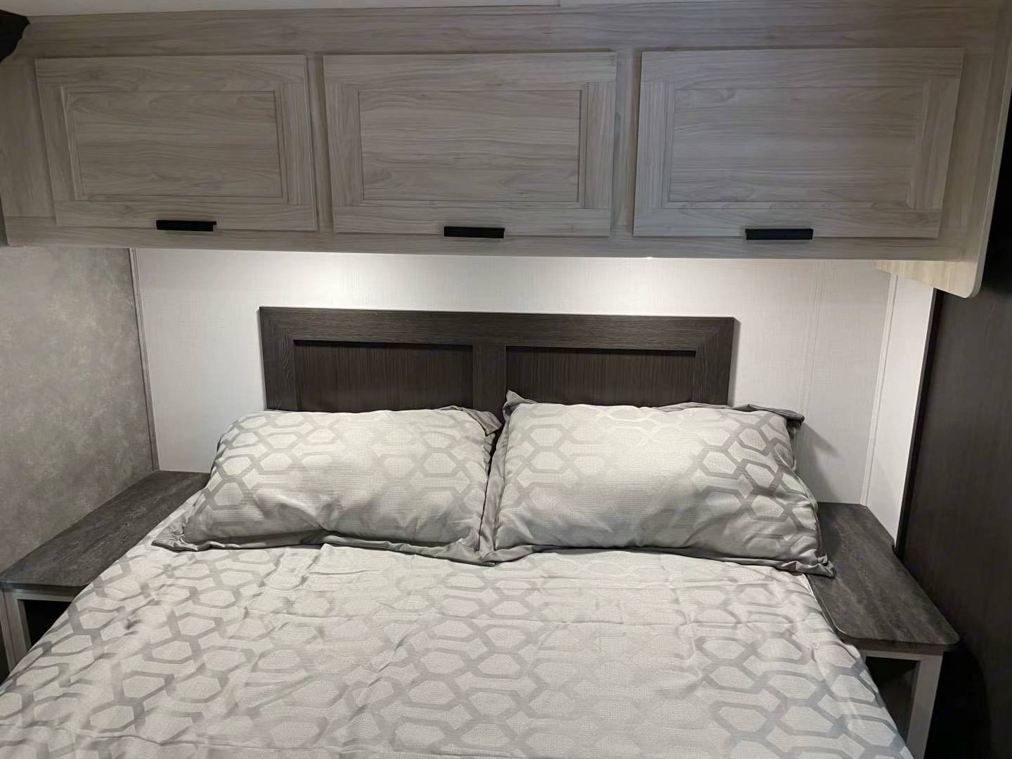 Modern RV rental bedroom featuring overhead storage cabinets, a dark headboard, and geometric patterned bedding.. Forest River Sunseeker LE 2022