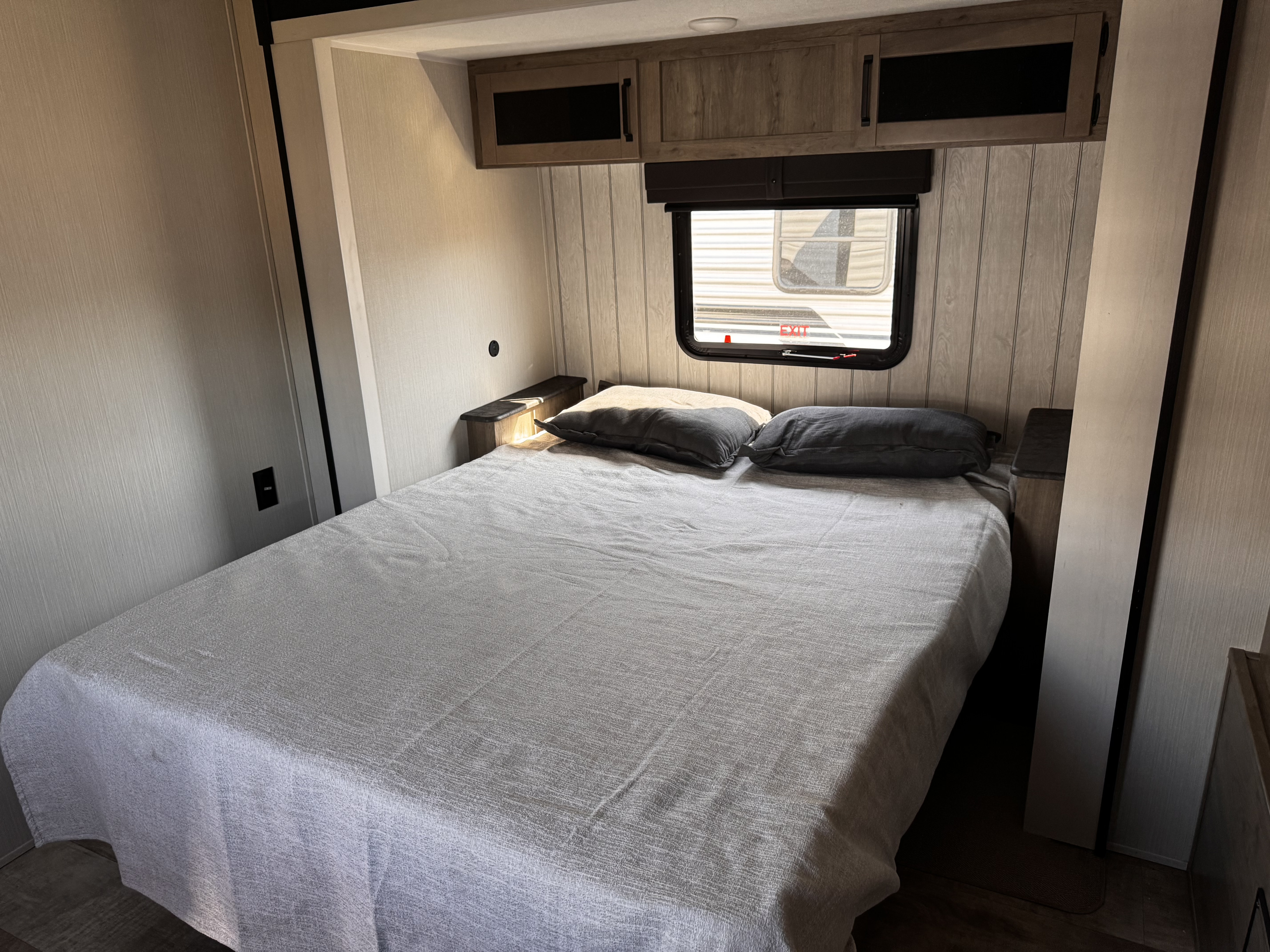 Comfortable bedroom in an RV rental, featuring a made bed with pillows, overhead cabinets, and a window.. Forest River Palomino Puma 2025