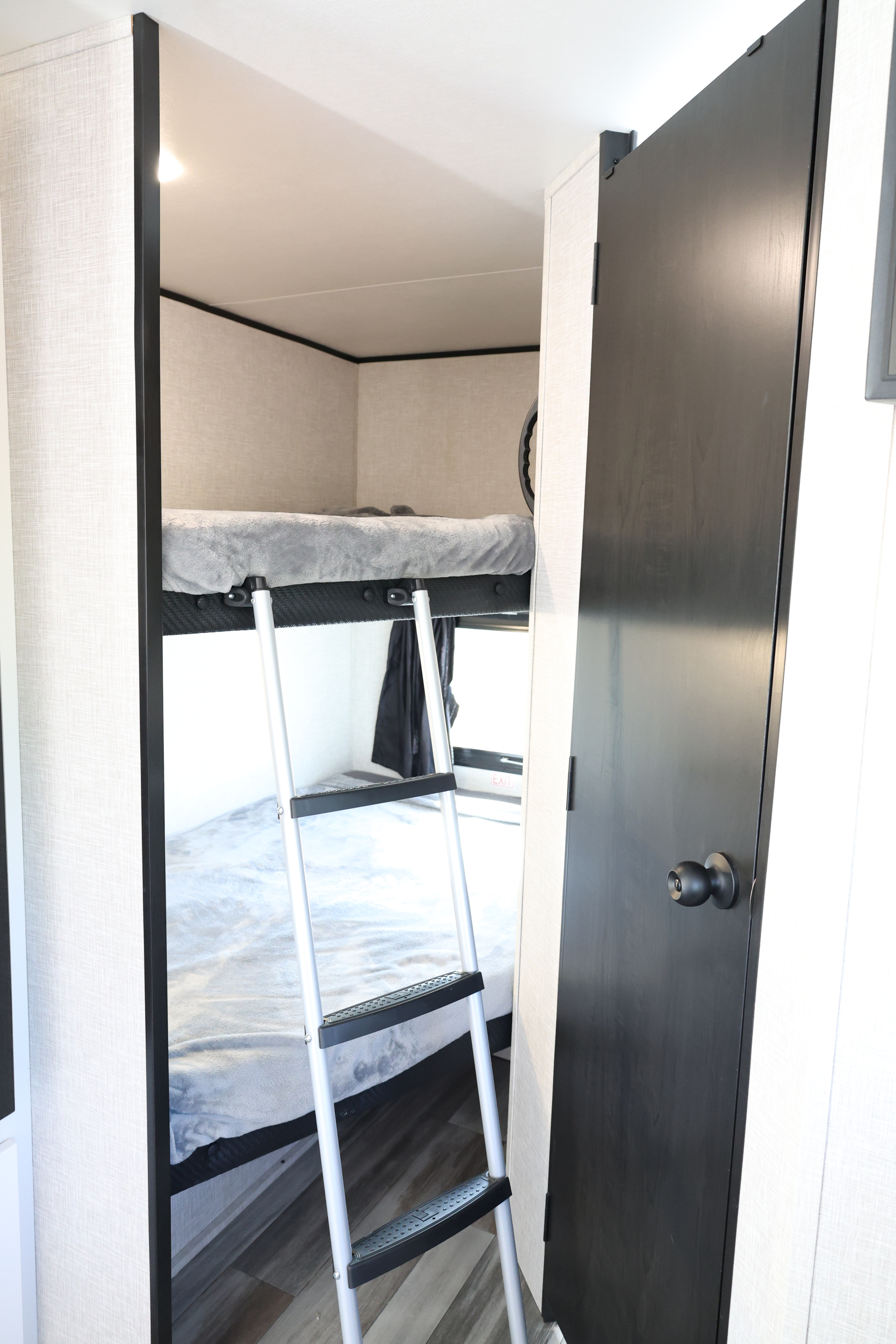 Inside an RV rental: a compact bunk bed area with a ladder, cozy grey bedding, and a dark door on the right.. Jayco Jay Flight SLX 2025