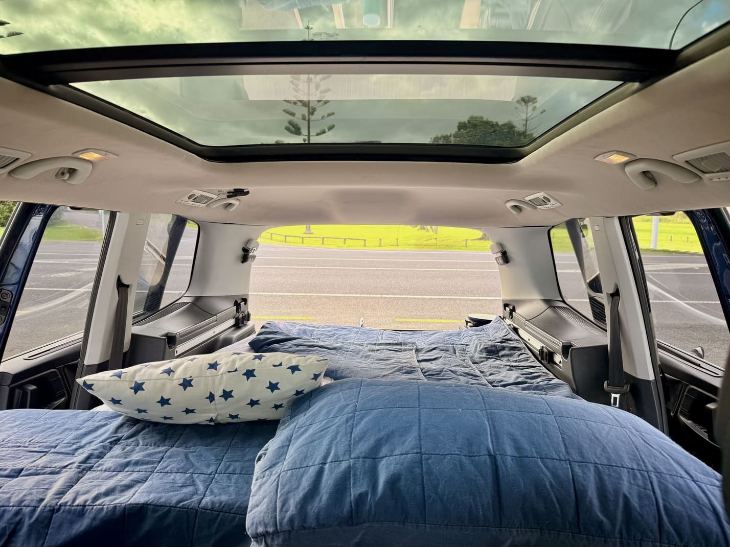 Comfy campervan RV rental bed with pillows under a panoramic skylight, perfect for a road trip setup.. Volkswagen Sharan 2012