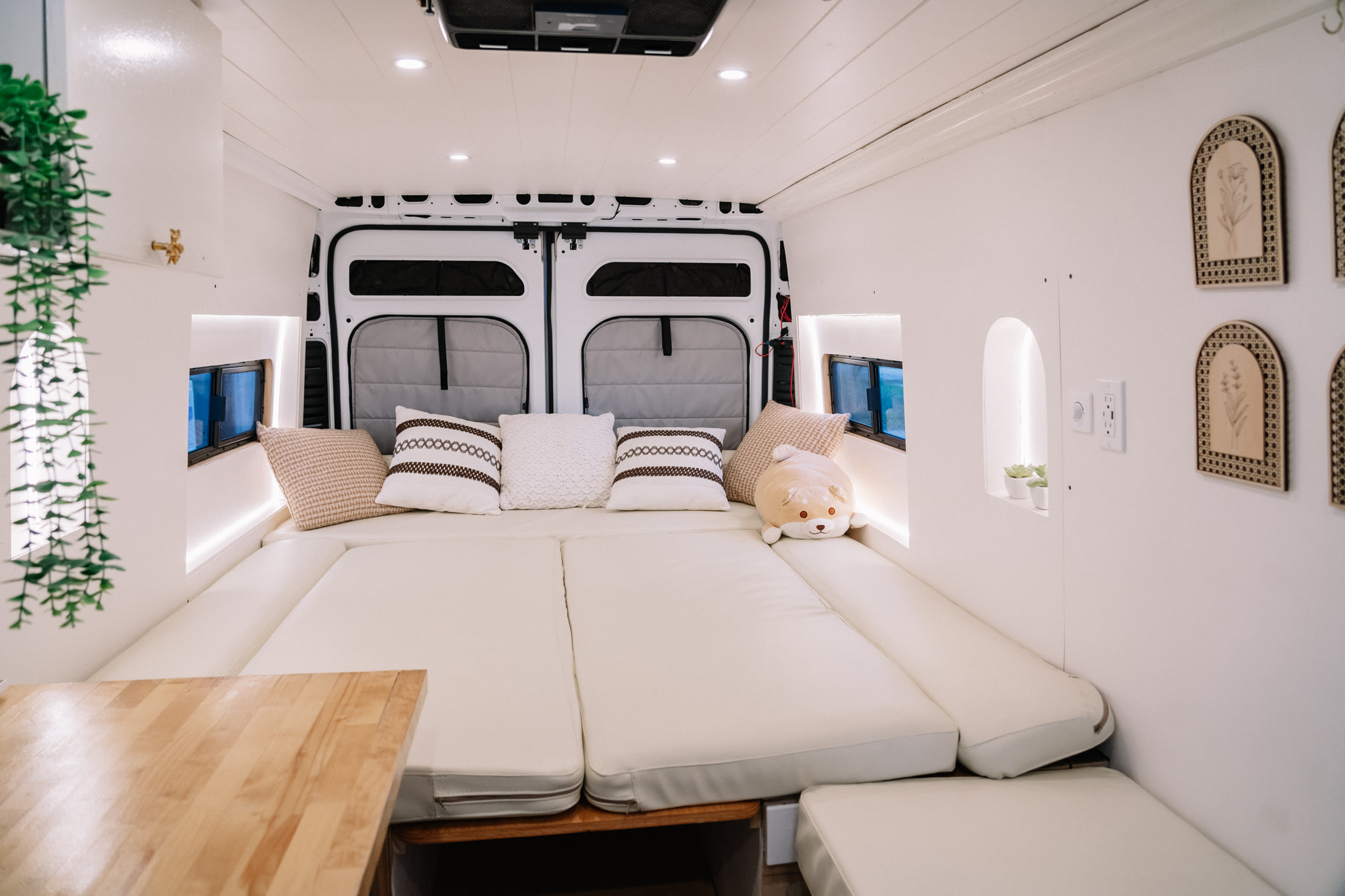 Interior of a modern rv rental camper van, featuring a spacious, cozy bed with cream cushions and stylish white decor.. Ram ProMaster 3500 2024