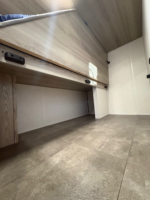 RV rental interior: A light wood-paneled bunk bed above a lower storage area, with textured grey tiled flooring.. Forest River Salem FSX 2025