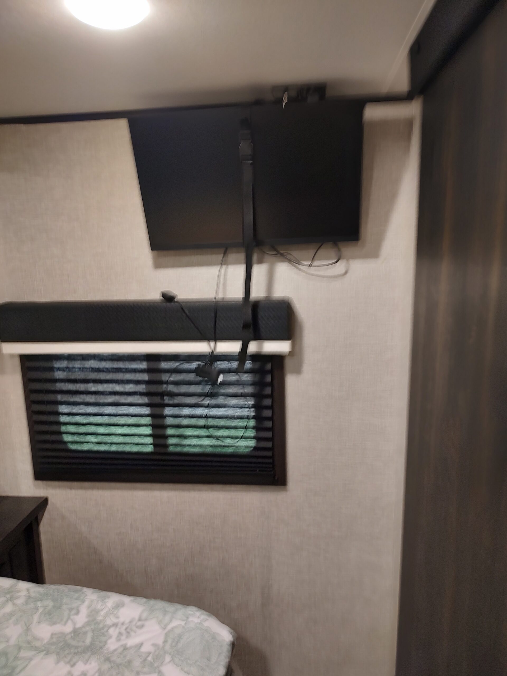 RV rental bedroom featuring a wall-mounted TV, window with blinds, and bed with light green floral bedding.. Jayco Jay Feather 2022