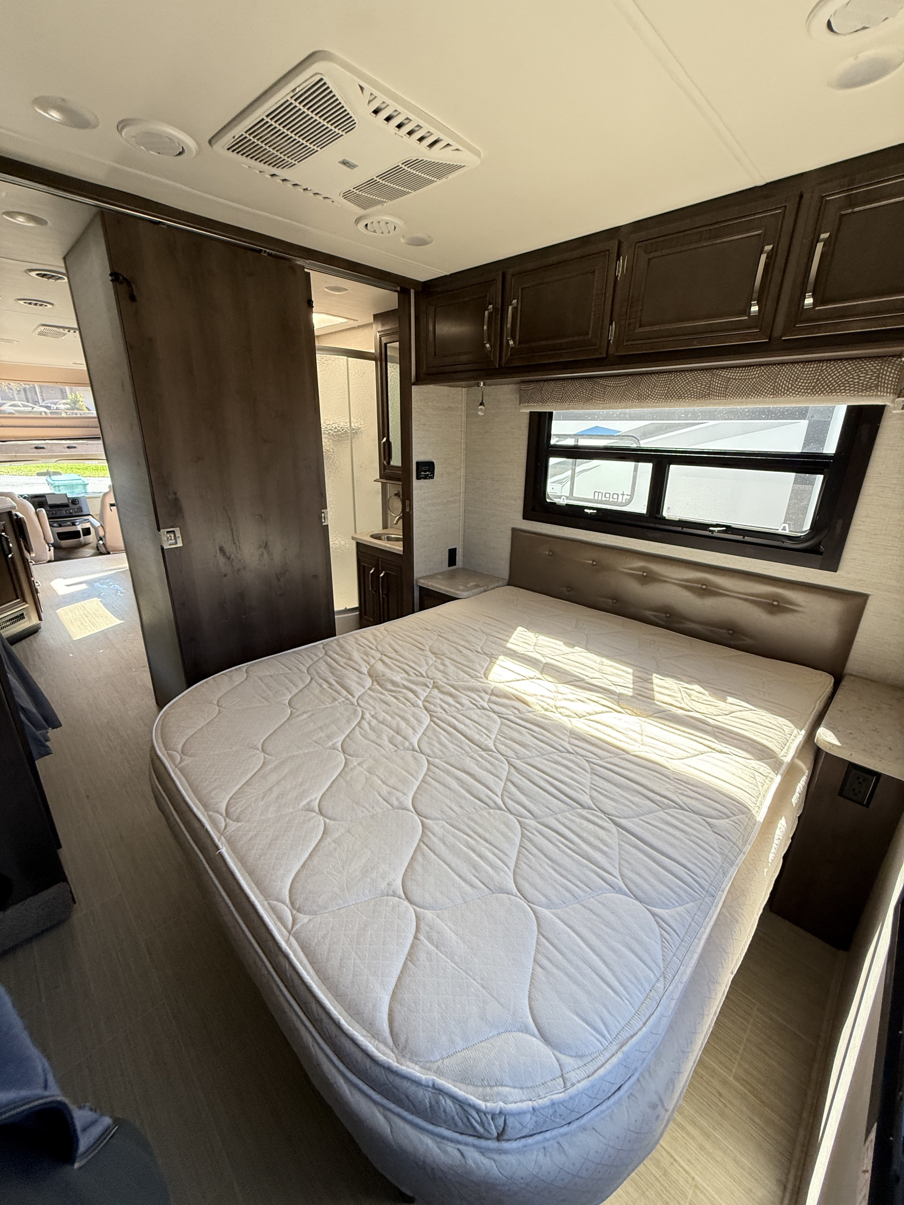 RV rental bedroom interior showing a white mattress, overhead cabinets, window, and sliding door to the bathroom. Bright.. Entegra Coach Esteem 2021