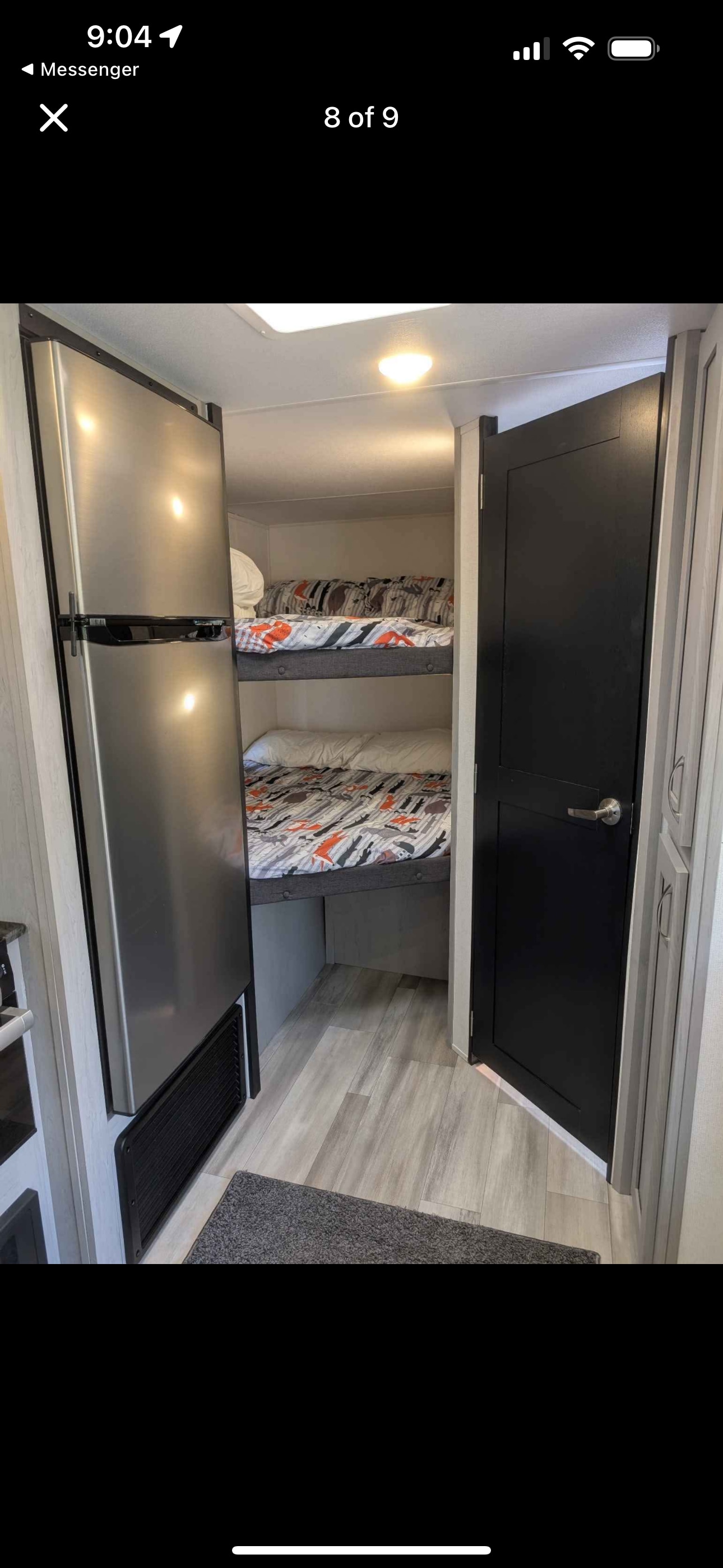 RV rental interior featuring a stainless steel refrigerator, cozy bunk beds with patterned bedding, modern wood-look floor, and a dark door.. Forest River Tracer 2022