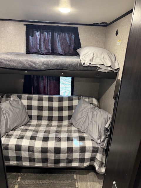 This rv rental offers comfy bunk beds: upper bed w/ grey blanket, lower futon w/ buffalo plaid. Great for families!. Jayco Jay Feather 2021
