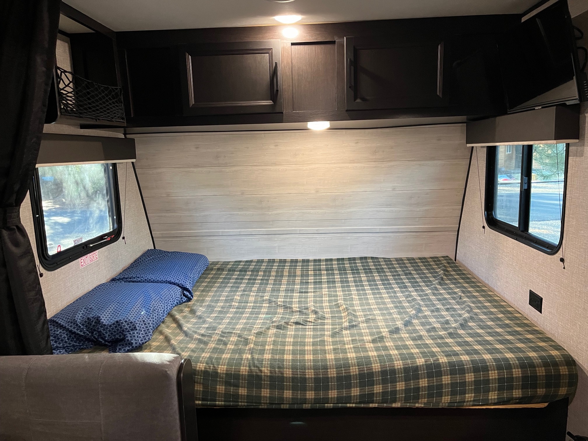 Inside an RV rental: a cozy bedroom with a plaid mattress, blue pillow, overhead cabinets, and windows.. Jayco Jay Flight SLX Baja Edition 2022