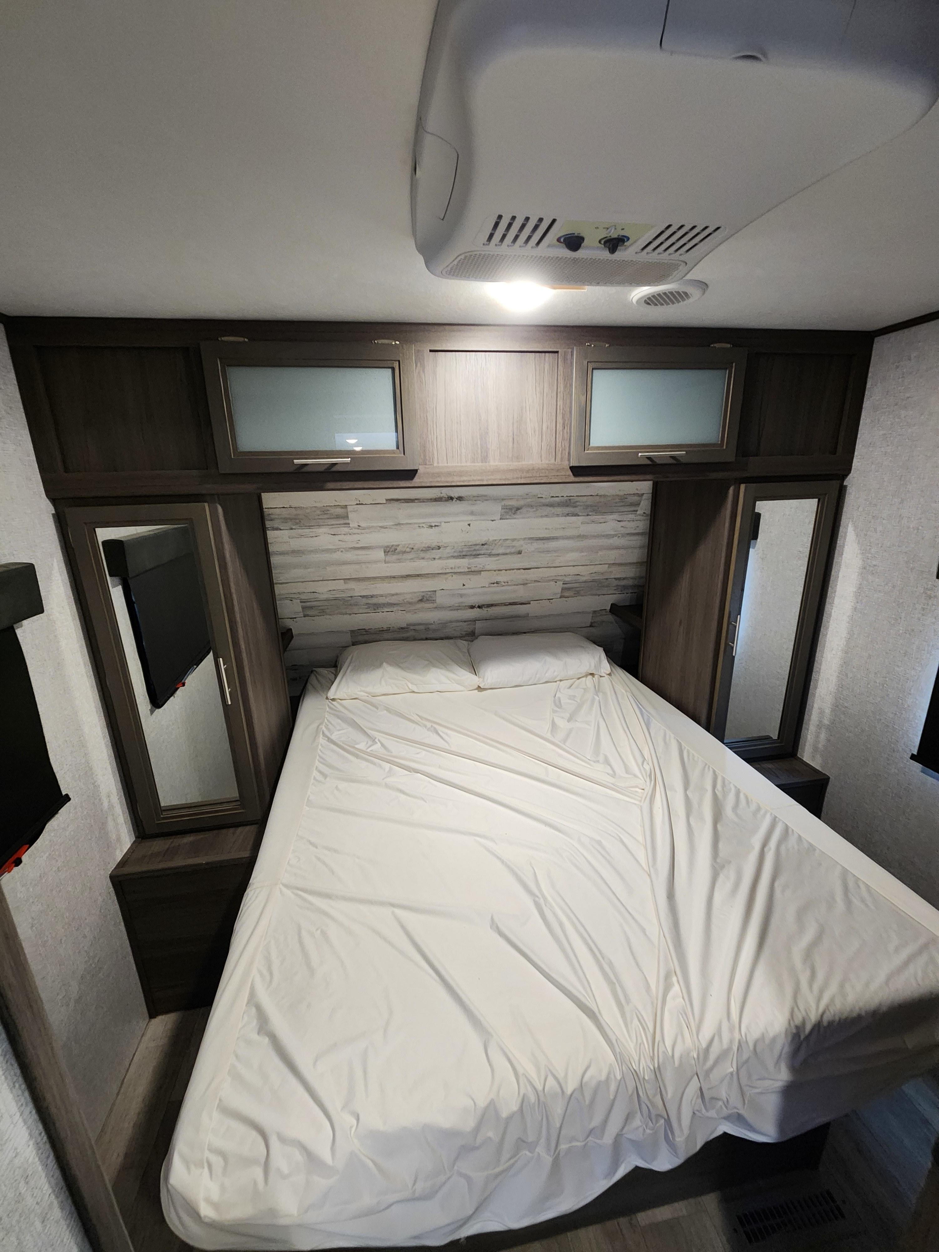 Cozy bedroom in an RV rental, featuring a bed with white sheets, built-in cabinetry, and ceiling AC unit.. Dutchmen Kodiak Ultra Lite 2021