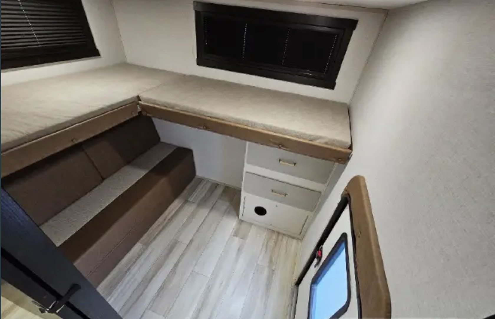 RV rental interior: L-shaped bunk beds above a sofa and storage drawers. Features wood flooring and an entry door.. Forest River Wildwood Heritage Glen HL 2025