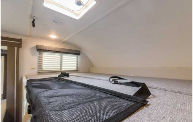 Inside an RV rental: Cozy overhead bunk bed with safety net, soft mattress, window blinds, and skylight. Ready for adventure.. Thor Four Winds 2025