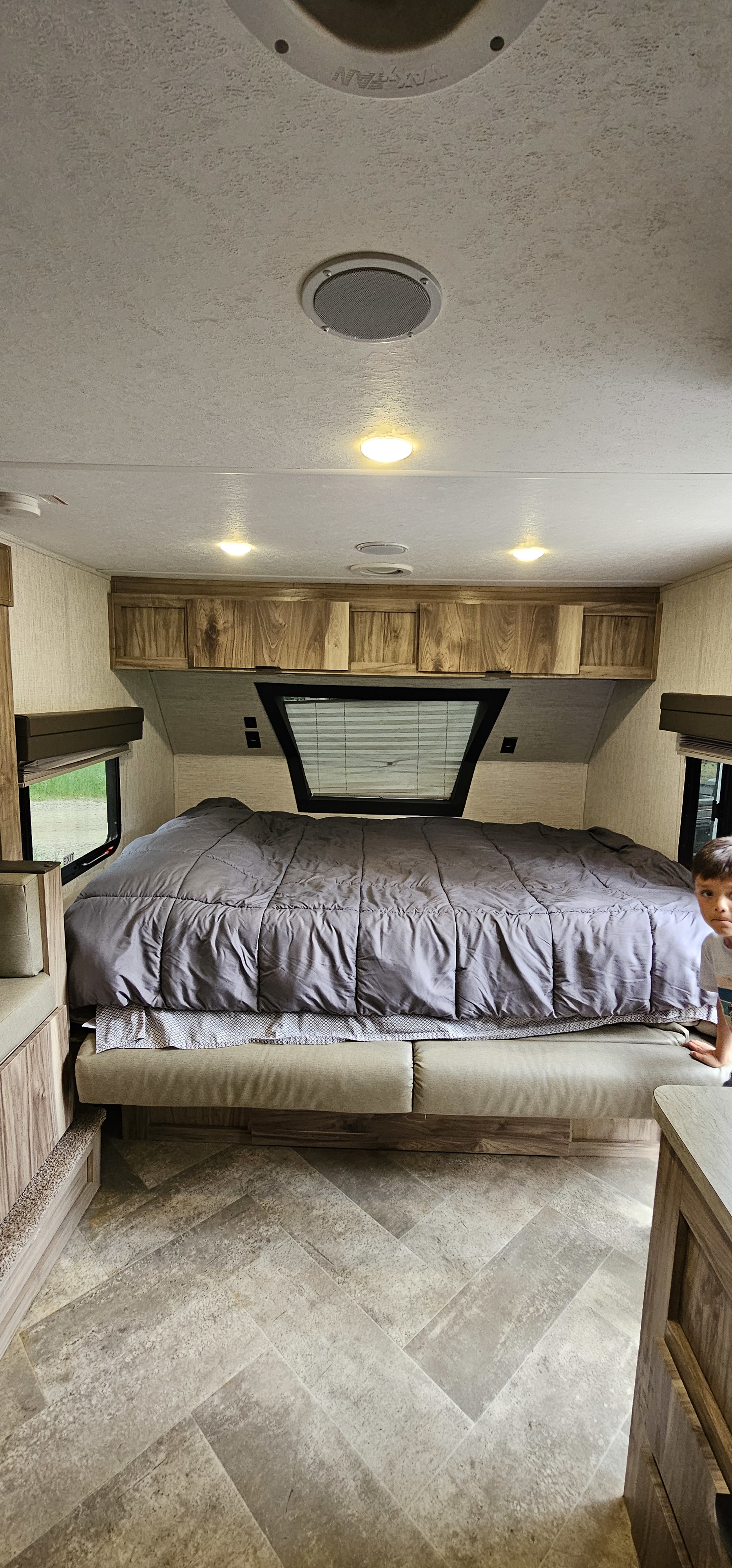 Spacious RV rental interior with a large bed, wooden cabinets, and herringbone flooring. A child peeks from the right.. Palomino 189BHS 2022