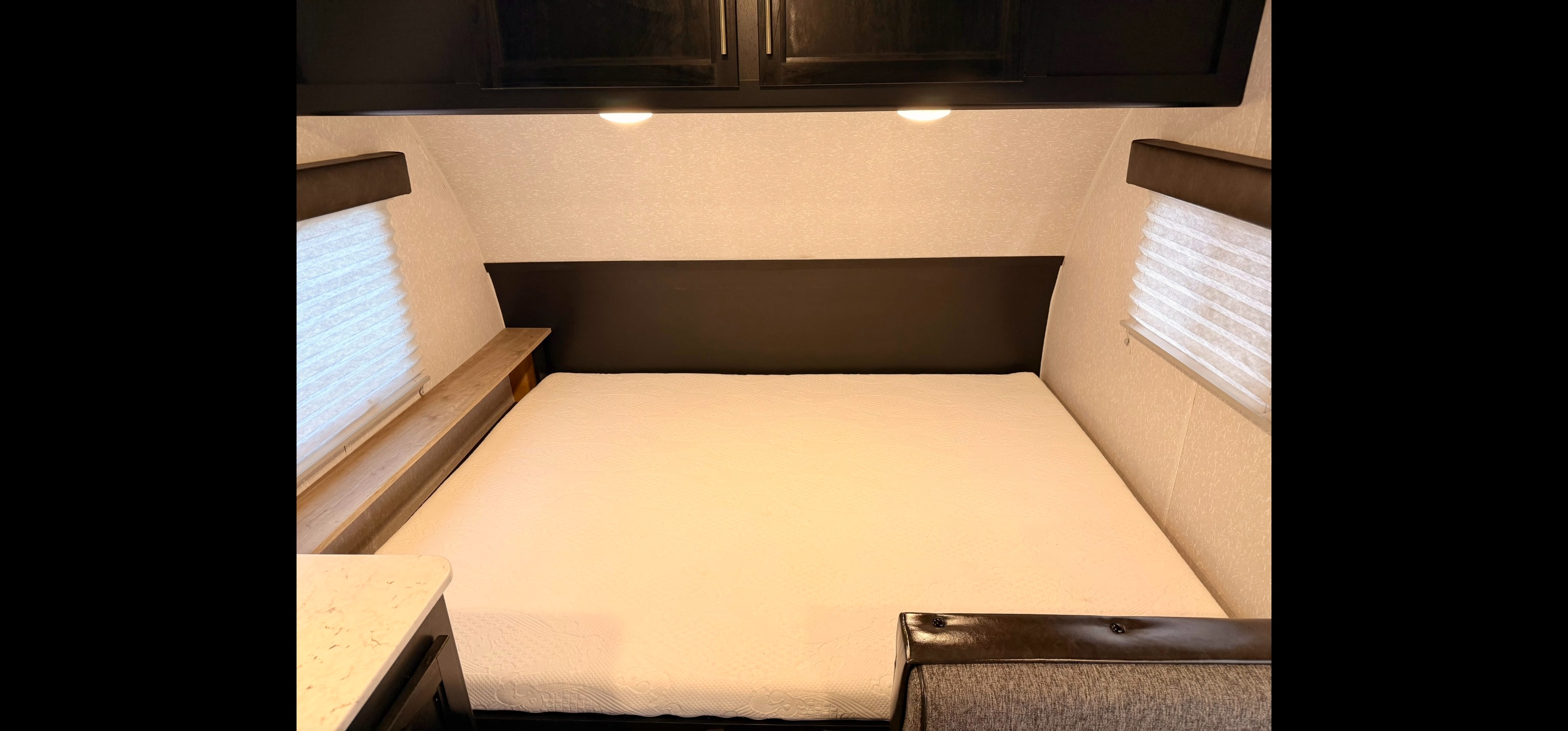 Cozy RV rental bedroom featuring a queen bed, overhead storage, side windows with blinds, and built-in shelf. Perfect for travel.. Forest River Cherokee Wolf Pup 2022