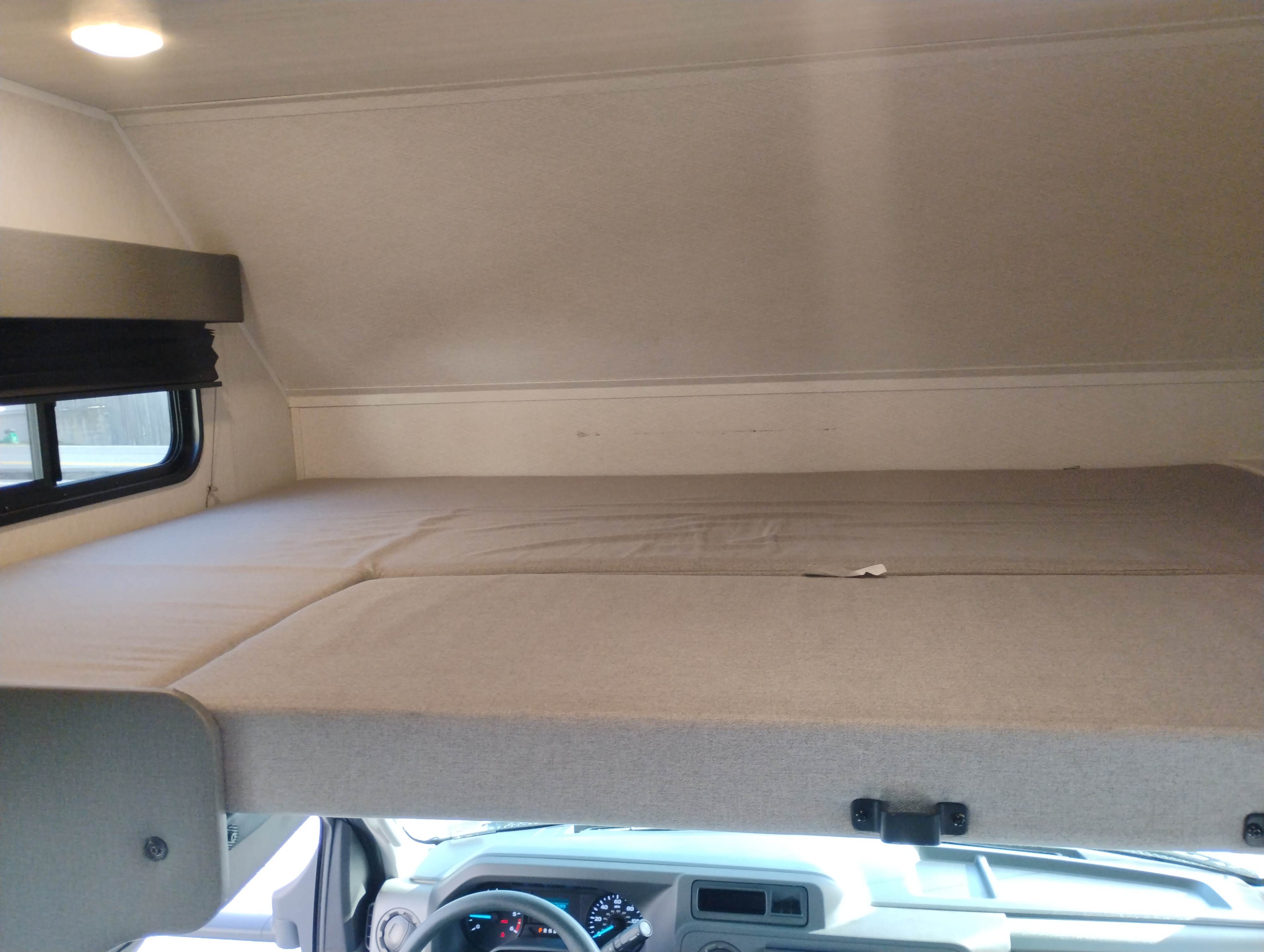 RV rental's cab-over bunk bed: A comfortable sleeping area above the driver's cabin, with a window to the left.. East to West Entrada 2026