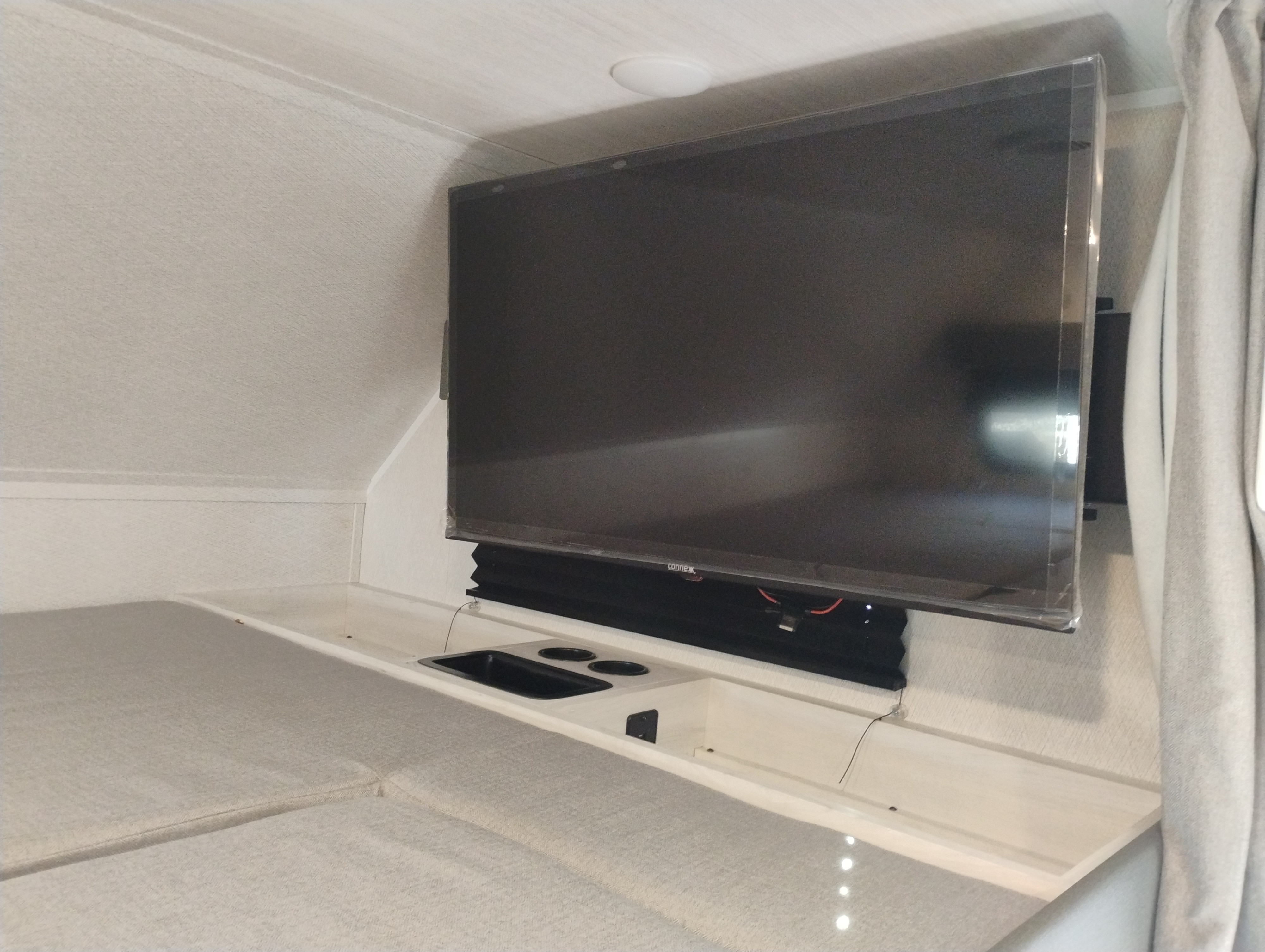 This RV rental's cozy interior features a mounted TV, integrated sink, and cup holders next to the comfortable bed.. East to West Entrada 2026